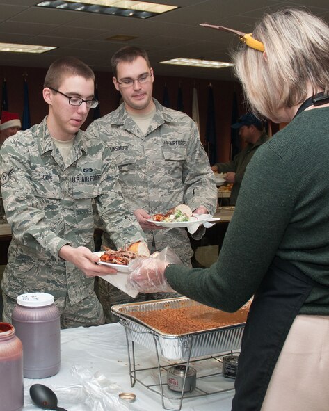 Charlotte Weilacher serves lunch to Airman Alec B. Cope (left) and Airman 1st Class Jude Hunsader, both assigned to the 66th Comptroller Squadron, at the 66th Air Base Group Holiday luncheon Dec. 12. Organizations within the group come together for a holiday luncheon each December in Building 1305. (U.S. Air Force photo by Mark Herlihy)