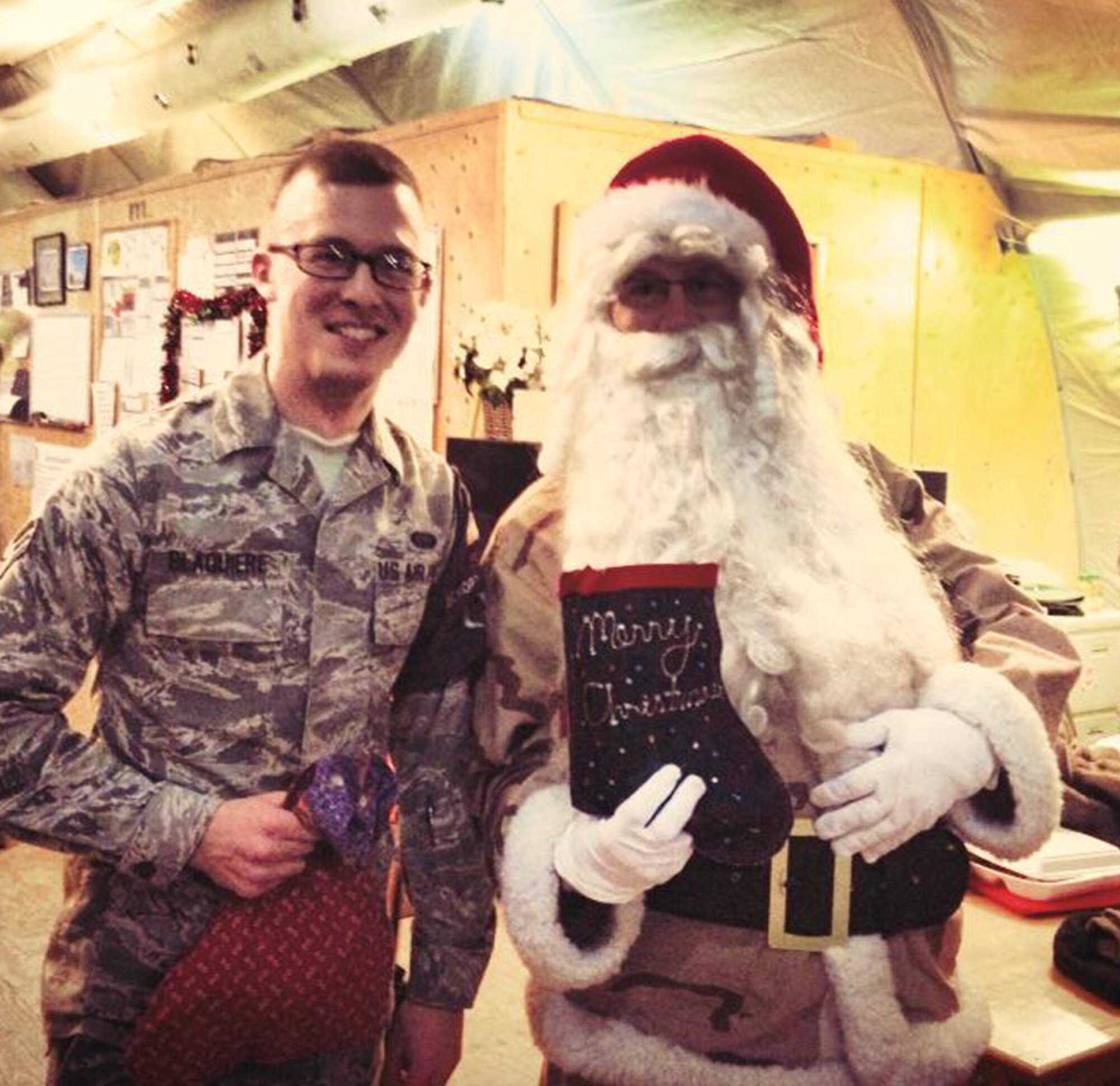U.S. Air Force Senior Airman Matthew Blaquiere, 376th Expeditionary Civil Engineer Squadron security escort flight, poses for a picture with Santa Claus after receiving a gift and a Christmas stocking from Santa Claus Dec. 7, 2013, at Transit Center at Manas, Kyrgyzstan. Santa Claus and his helpers paid a special visit to the 376th ECES during their morning formation to spread holiday cheer to the deployed Airmen. Blaquiere is a Clarkston, Mich. native, deployed from RAF Mildenhall, England. (Courtesy photo) 