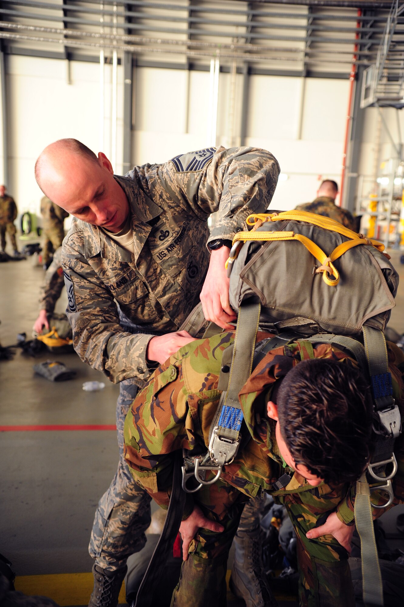 Senior Master Sgt. Terrance Hyland, 435th Security Forces Squadron, assists a fellow paratrooper with his parachute during Jump Week, Dec. 16, 2013, Ramstein Air Base, Germany. International Jump Week started with a bang this year as Santa Claus joined service members from different branches of the U.S. along with NATO forces. (U.S. Air Force photo/Senior Airman Hailey Haux)