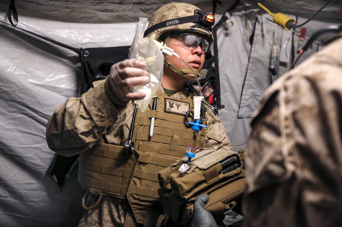 Navy Petty Officer 3rd Class Ruben E. Ramirez lifts an IV bag to begin the flow of liquids to a wounded Marine during Exercise Steel Knight 2014 on Marine Corps Air Ground Combat Center, Twentynine Palms, Calif., Dec. 13, 2013. Ramirez, a hospital corpsman, is assigned to Headquarters Company, 1st Battalion, 5th Marines.