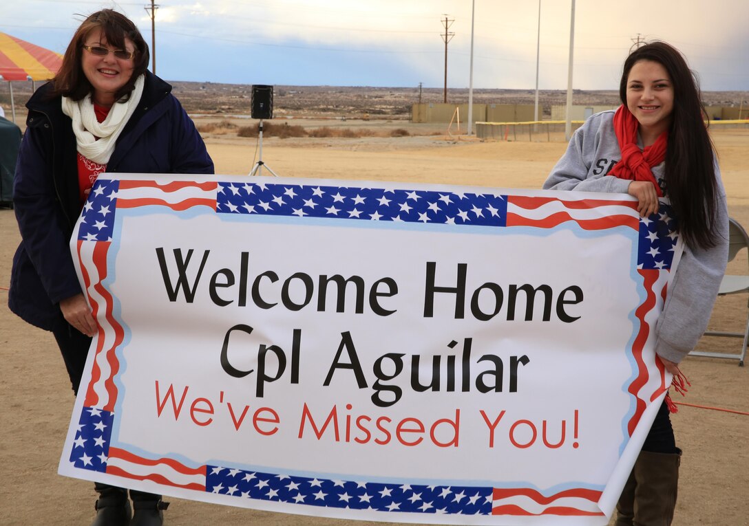 Theresa aguilar, mother of Cpl. Brian Aguilar, armorer, Company L, 3rd Battalion, 7th Marine Regiment, and her daughter, Samantha Aguilar, await the return of Cpl. Aguilar with a sign welcoming him back the Combat Center's Del Valle field Dec. 19, 2013.