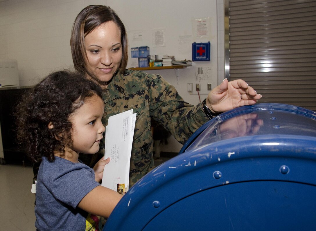 Gunnery Sgt. Virgen Jenkins, postal chief, shows Rosaleah Cruz, 3, how to place her letter in the mailbox at the Marine Corps Base Hawaii post office, Dec. 12, 2013. The children from Kupulau Child Development Center received a mini tour of the base post office. They also brought holiday pictures to mail to family members. The Marines from the base post office taught the children how to stamp the official processing date on each letter and insert them into a mailbox. (U.S. Marine Corps photo by Kristen Wong)