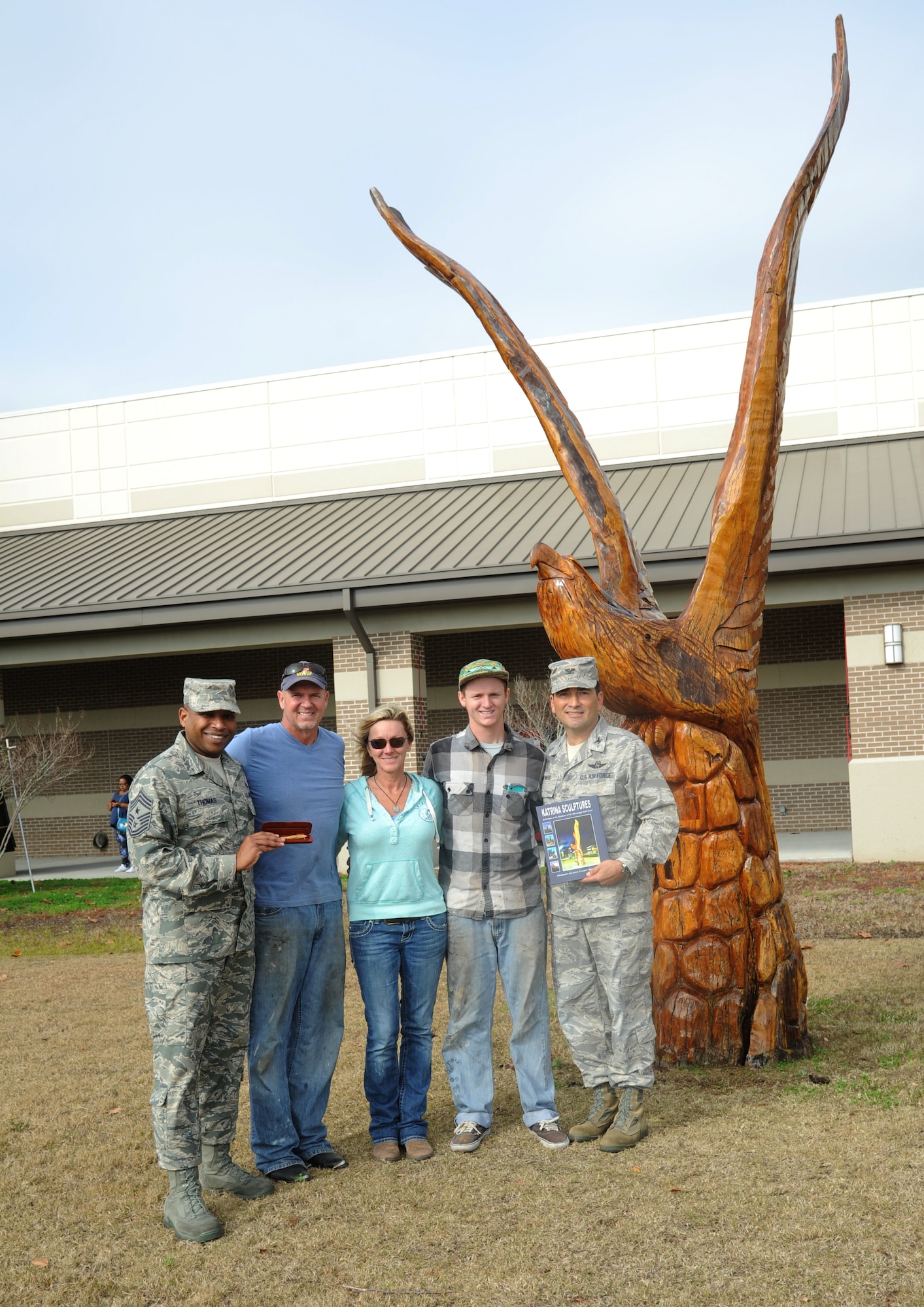 Chief Master Sgt. Farrell Thomas, 81st Training Wing command chief, and Col. René Romero, 81st TRW vice commander, takes a photo with Florida sculptor, Marlin Miller, and his wife, Rene, and son Preston, while standing in front of the eagle Miller sculpted in front of the exchange Dec. 20, 2013, at Keesler Air Force Base, Miss.  Miller has sculpted dozens of wooden figures from Hurricane Katrina-battered trees along the Gulf Coast, including the eagle in front of the exchange.  (U.S. Air Force photo by Kemberly Groue)