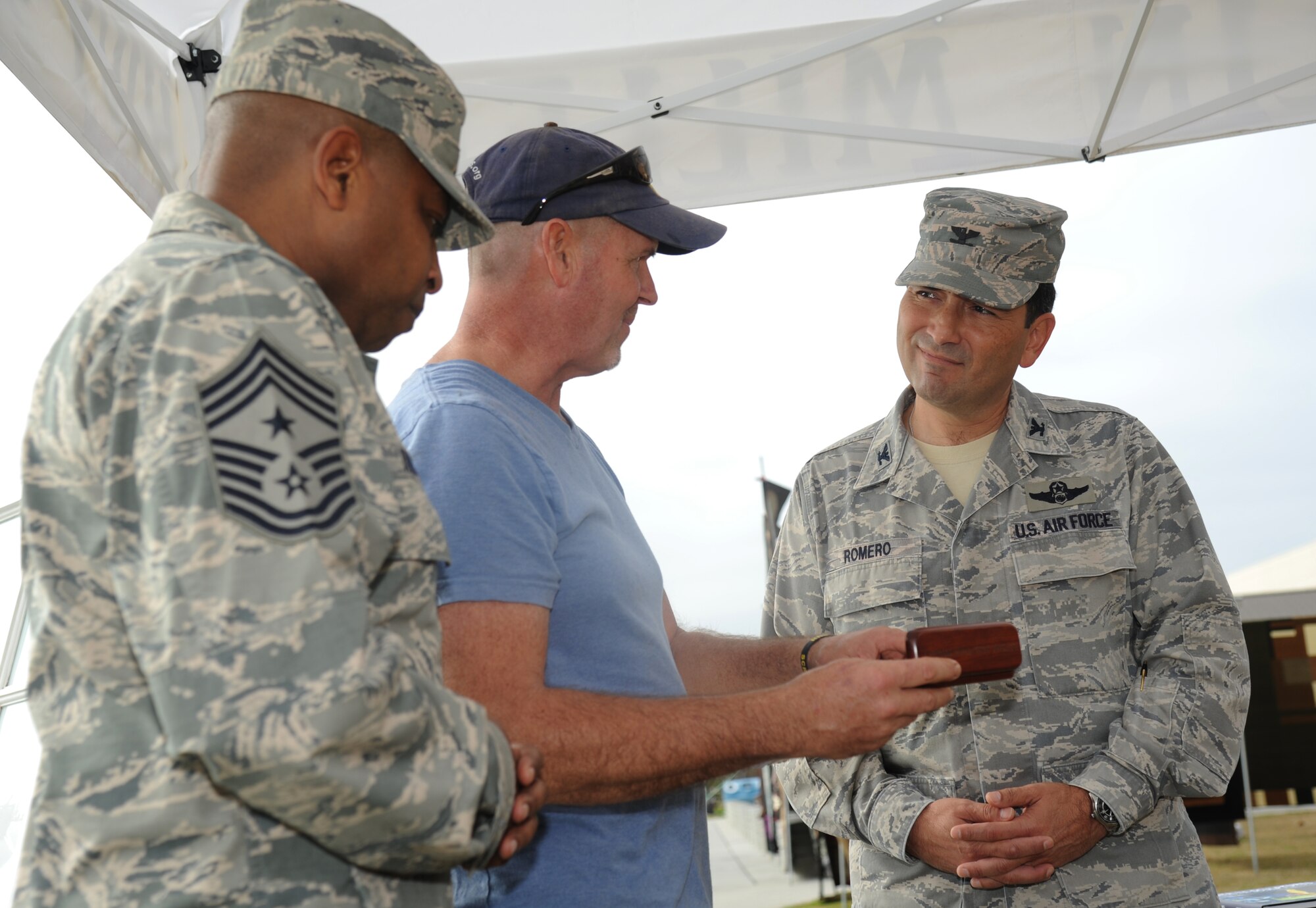Chief Master Sgt. Farrell Thomas, 81st Training Wing command chief, looks on as Marlin Miller, Florida sculptor, presents an oak pen to Col. René Romero, 81st TRW vice commander, Dec. 20, 2013, in front of the exchange, at Keesler Air Force Base, Miss.  Miller has sculpted dozens of wooden figures from Hurricane Katrina-battered trees along the Gulf Coast, including the eagle in front of the exchange.  (U.S. Air Force photo by Kemberly Groue)