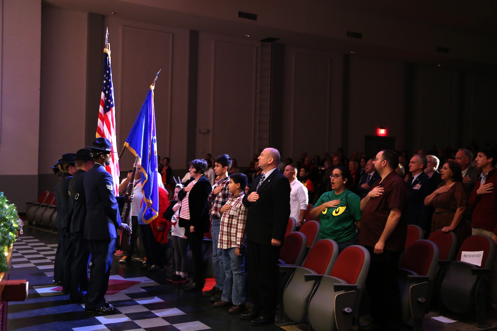 Audience members show respect to the country by placing their hand over their heart or standing at attention while military training instructors present the colors Dec. 17 at the Joint Base San Antonio-Lackland Bob Hope Theater. (U.S. Air Force photo by Airman 1st Class Lincoln Korver)