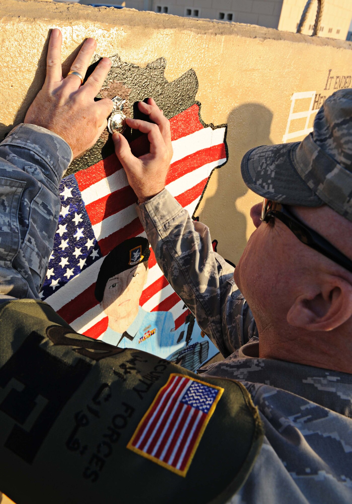 Chief Master Sgt. Dewey Hansford, 386th Expeditionary Security Forces Squadron chief manager, donates his SFS badge to a 2005 tribute painting of Airman 1st Class Elizabeth Jacobson, undisclosed location Southwest Asia. After noticing sun damage and chipped paint Moore decided to resuscitate the beauty it once had. She is the first Security Forces Airman to die in Operation Iraqi Freedom. She is also the first female Airman killed in the line of duty in support of OIF. (U.S. Air Force photo by Senior Airman Desiree W. Moye)