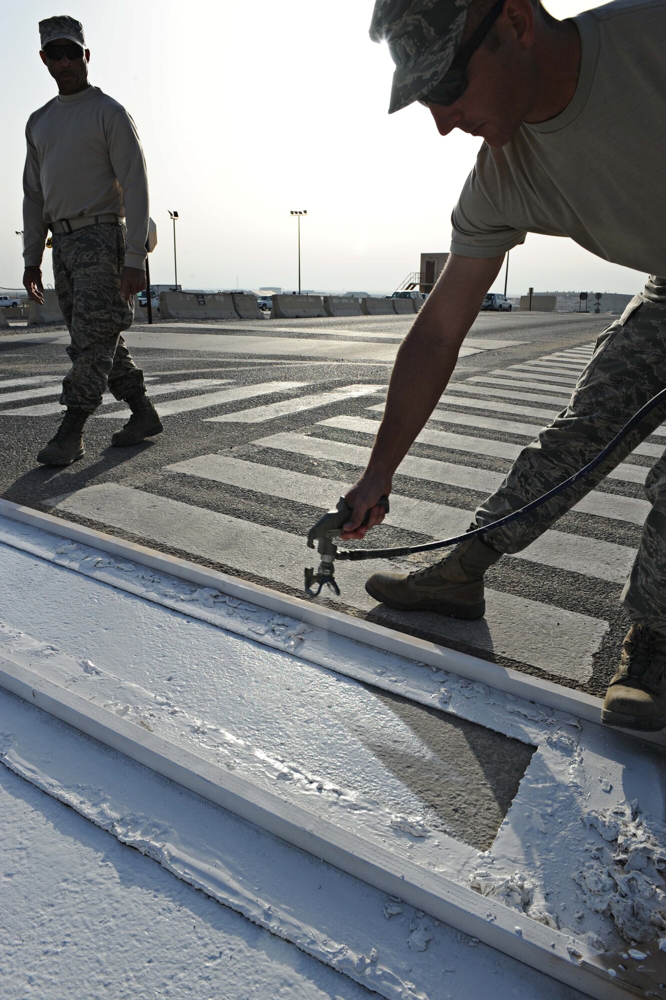Technical Sgt. Joseph Hodges repaints a pedestrian cross walk as Staff Sgt. Adrian Doss looks on, both from 386th Expeditionary Civil Engineer Squadron structures, undisclosed location Southwest Asia. Base improvements are consistently ongoing on The Rock. (U.S. Air Force photo by Senior Airman Desiree W. Moye)