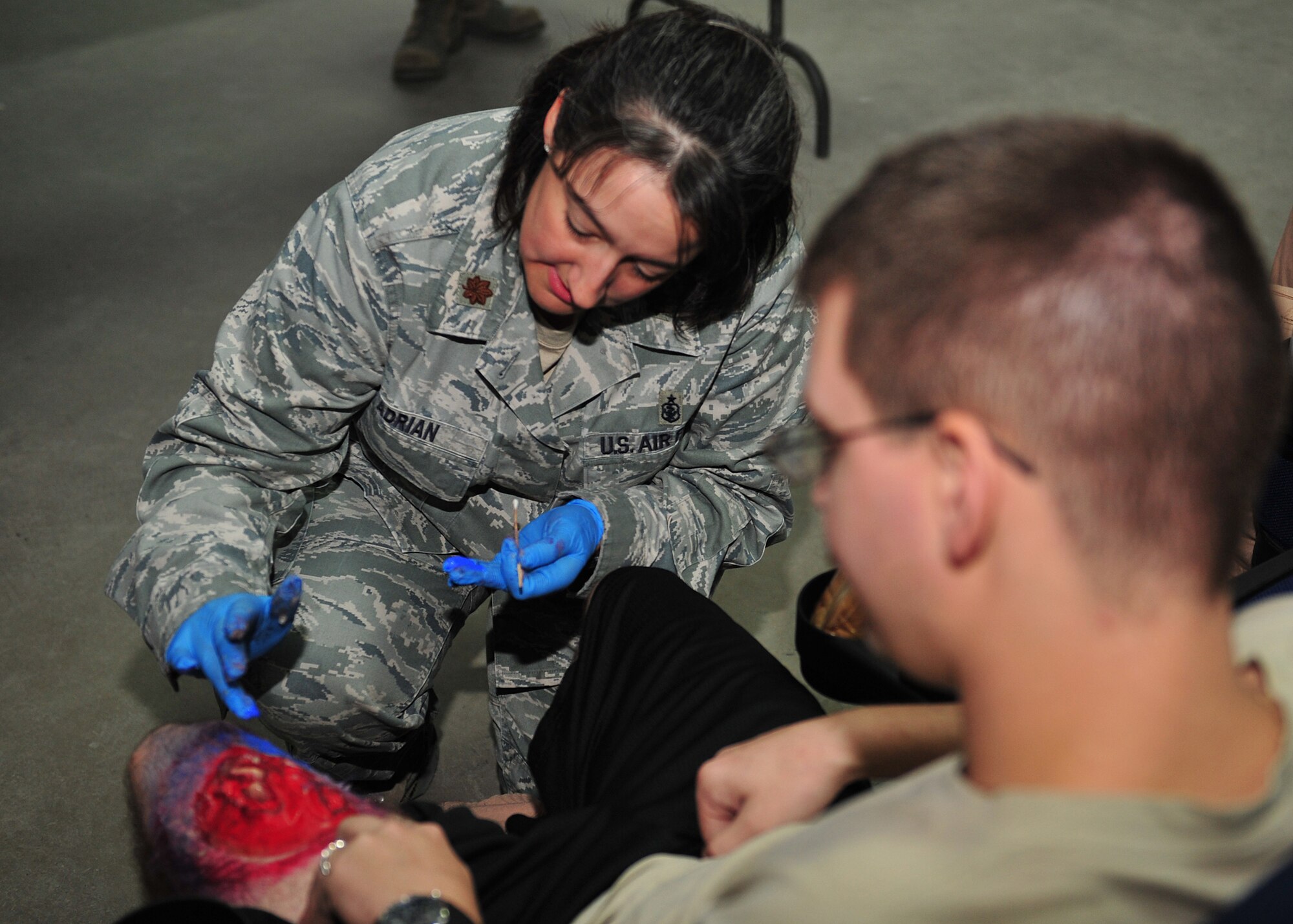 Air Force Maj. Dana Adrian, who is assigned to the 380th Expeditionary Medical Group moulage team, applies make-up to Air Force Staff Sgt. Charles Nestor, a communications system operator assigned to the 968th Expeditionary Airborne Air Control Squadron, to simulate a broken leg at an undisclosed location in Southwest Asia, Dec. 19, 2013. (U.S. Air Force photo by Staff Sgt. Michael Means/Released)