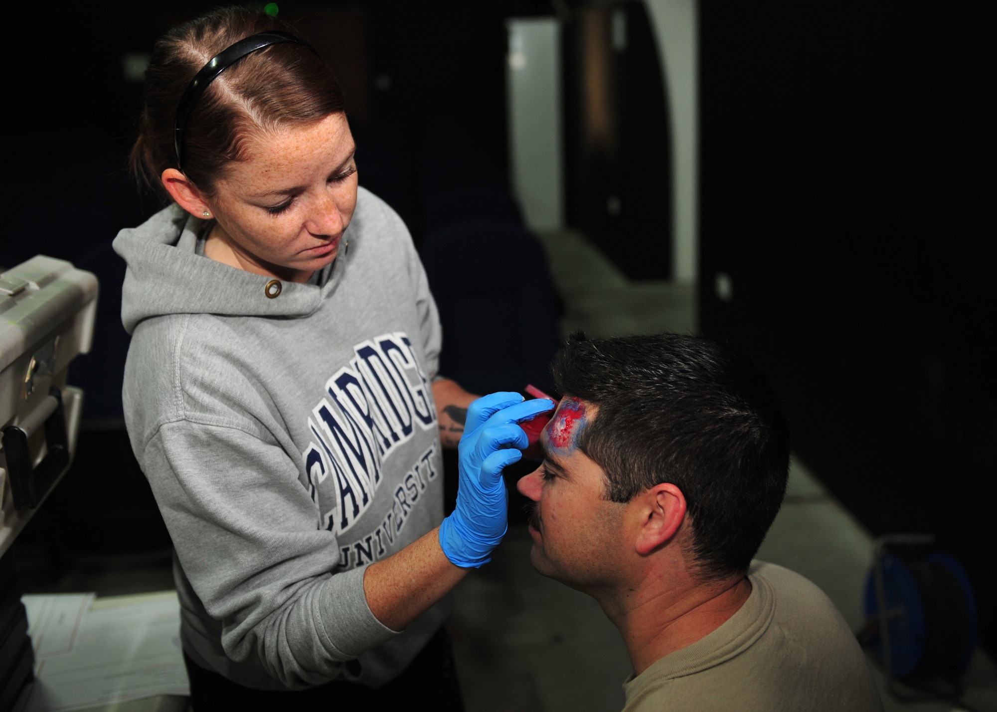 Air Force Staff Sgt. Samantha, who is assigned to the 380th Expeditionary Medical Group moulage team, applies make-up to Air Force 1st Lt. Calvin Collins, an air weapons officer assigned to the 968th Expeditionary Airborne Air Control Squadron, to simulate a head injury at an undisclosed location in Southwest Asia, Dec. 19, 2013. (U.S. Air Force photo by Staff Sgt. Michael Means/Released)