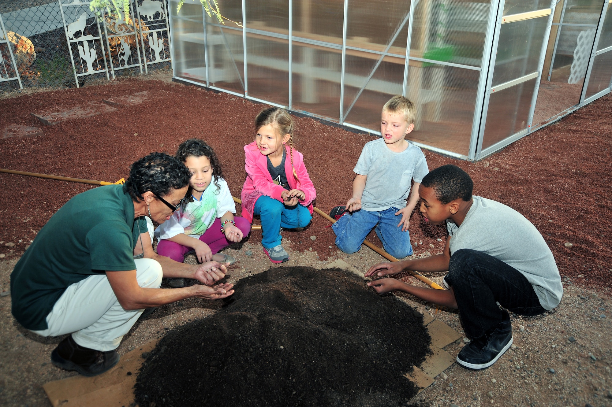Children at the School Age Program and program leaders take photos standing in front of the finished greenhouse at Davis-Monthan Air Force Base, Ariz., Dec. 19, 2013. A greenhouse is a structural building with different types of covering materials, such as a glass, or plastic roofs and glass or plastic walls; it heats up because incoming visible sunshine is absorbed inside the structure. (U.S. Air Force photo by Airman 1st Class Betty R. Chevalier/Released)