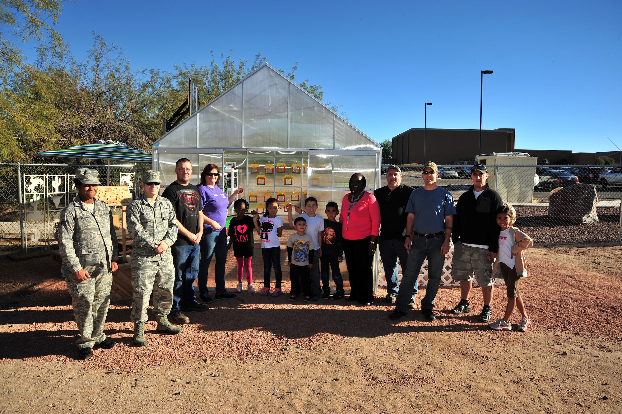 Children at the School Age Program and program leaders take photos standing in front of the finished greenhouse at Davis-Monthan Air Force Base, Ariz., Dec. 19, 2013. A greenhouse is a structural building with different types of covering materials, such as a glass, or plastic roofs and glass or plastic walls; it heats up because incoming visible sunshine is absorbed inside the structure.(U.S. Air Force photo by Airman 1st Class Betty R. Chevalier/Released)