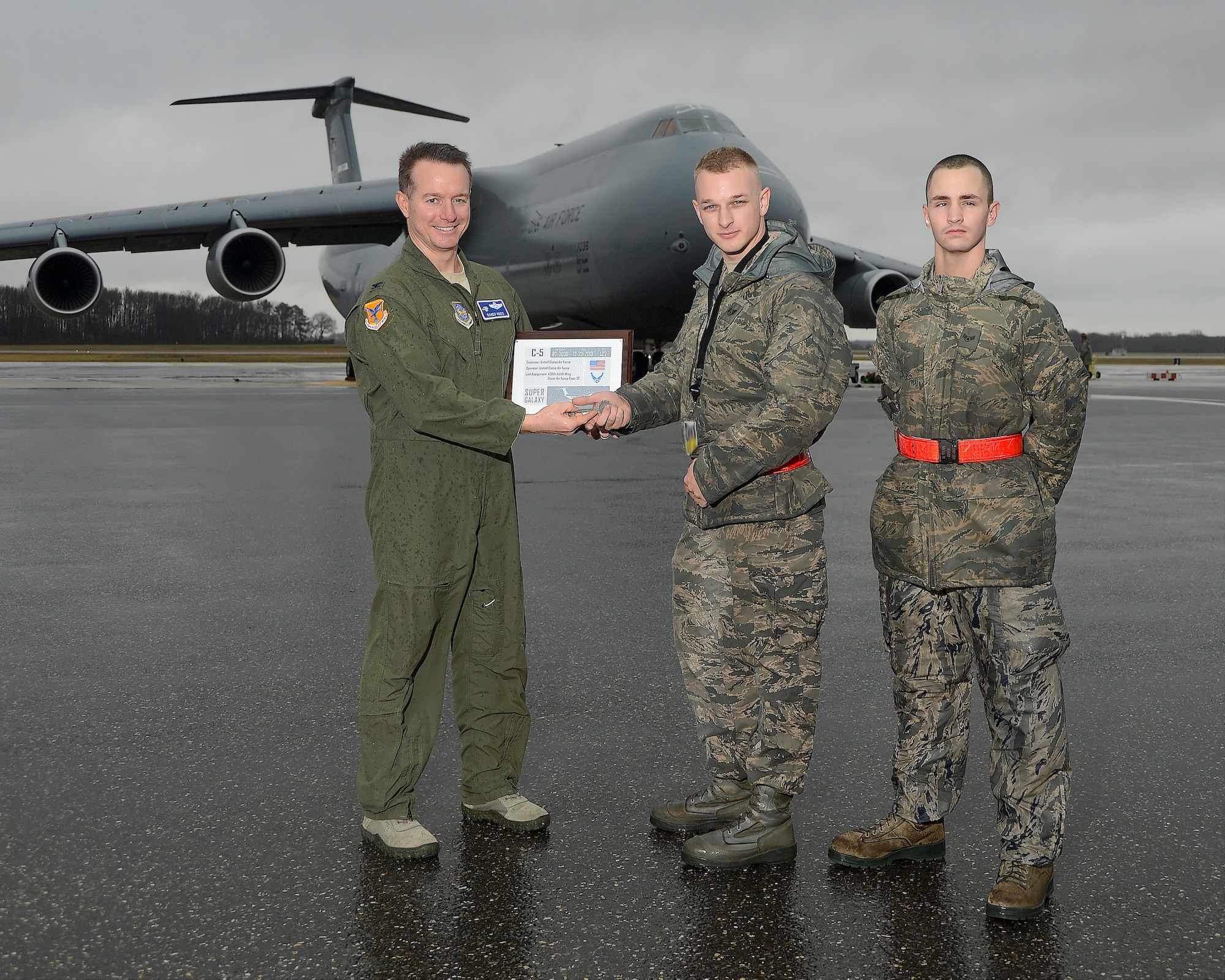 Col. Randy Huiss, vice wing commander of the 436th Airlift Wing, (left) presents a symoblic key and certificate for the 16th remanufactured C-5 Galaxy, serial # 87-0036, to Staff Sgt. Joshua Townsend, the aircraft's dedicated crew chief, upon arrival at Dover Air Force Base, Del., on Dec. 23, 2013. SSgt. Townsend is the dedicated crew chief for the aircraft and is joined by the assistant crew chief, Airman 1st Class Nathan Ryan, for the presentation. The aircraft was formerly operated by the 60th Air Mobility Wing, 349th Air Mobility Wing (Air Force Reserve Command), Travis AFB, Calif., and still wears markings for the unit. Although the aircraft has completed the major airframe, engine and avionics upgrades for the C-5M configuration, it will soon be sent to Stewart Air National Guard Base, N.Y. for a complete interior upgrade. Upon completion of the interior upgrade then the aircraft will be considered fully mission configured and take on the C-5M Super Galaxy name. 87-0036, joins 15 additonal upgraded C-5s at the 436th Airlift Wing, currently the sole front-line transport Wing to operate the Super Galaxy. This image has been digitally altered to blur an identification badge(U.S. Air Force photo/Greg L. Davis)