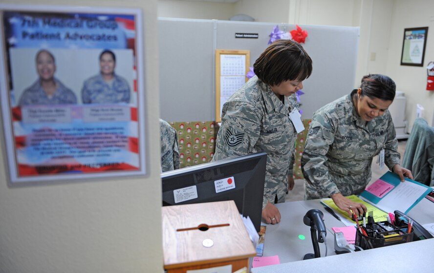 U.S. Air Force Tech. Sgt. Suzette Miller and Staff Sgt. Soni Boose, 7th Medical Group, review paperwork at the patient administration office Dec. 5, 2013, at Dyess Air Force Base, Texas. The flyer on the left is one of many located by the window of each section of the medical group. These flyers contain pictures and contact information of each patient advocate. (U.S. Air Force photo by Airman 1st Class Kedesha Pennant)