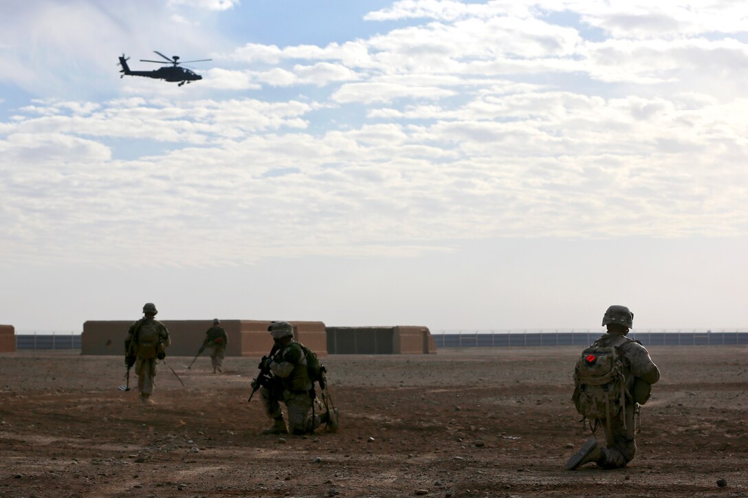 An AH-64 Apache attack helicopter flies above as U.S. Marines learn how to mark improvised explosive devices on Camp Leatherneck in Afghanistan's Helmand province, Dec. 20, 2013.