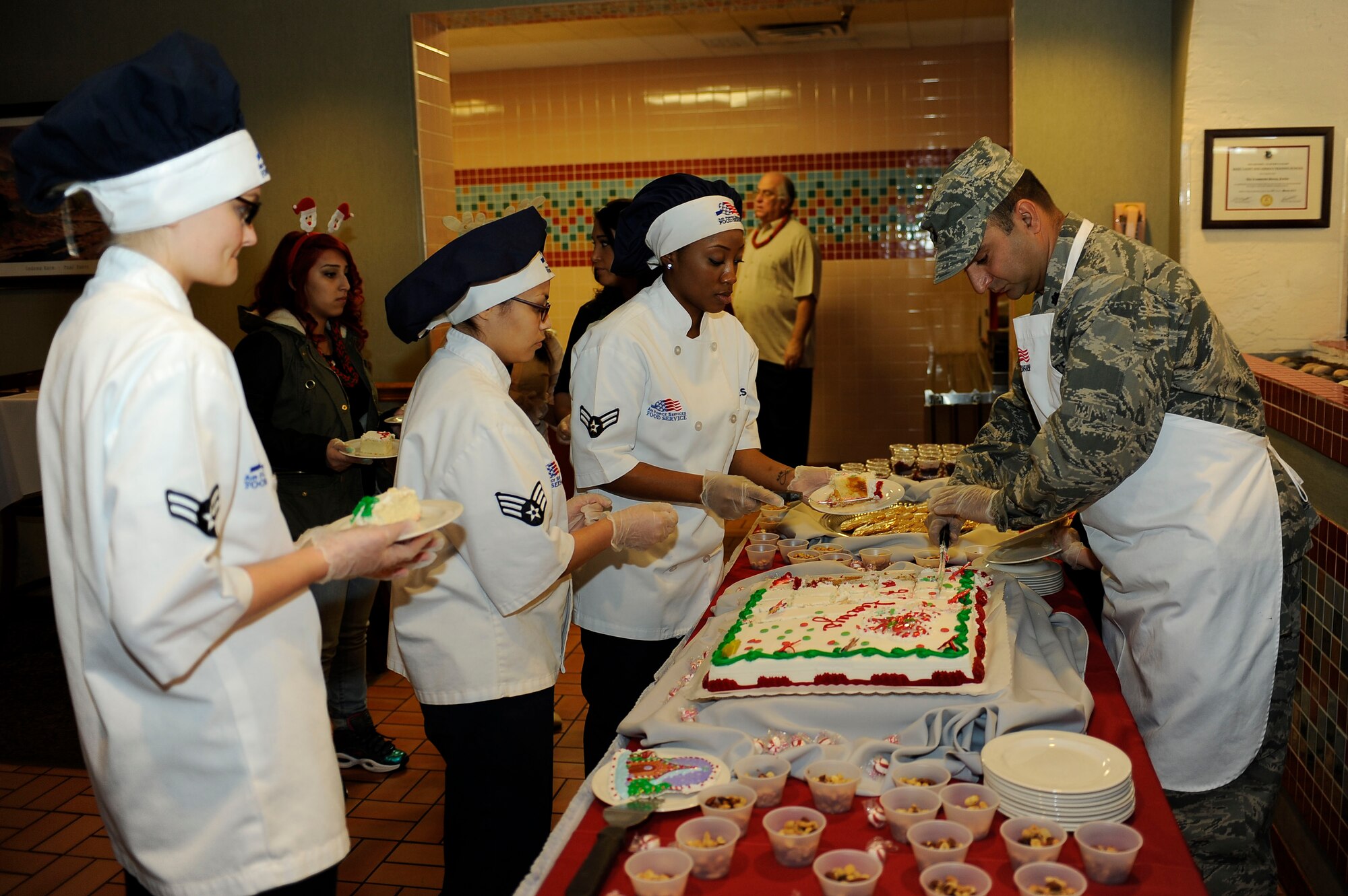 Lt. Col. Cameron Dadgar, 549th Combat Training Squadron commander, and 99th Force Support Squadron Airmen prepare servings of cake for guests at the Crosswinds Dining Facility during a holiday meal Dec. 25, 2013, at Nellis Air Force Base, Nev. The entire food service team prepared the meal while leadership from the U.S. Air Force Warfare Center, 57th Wing and 99th Air Base Wing served guests. (U.S. Air Force photo by Airman 1st Class Timothy Young)