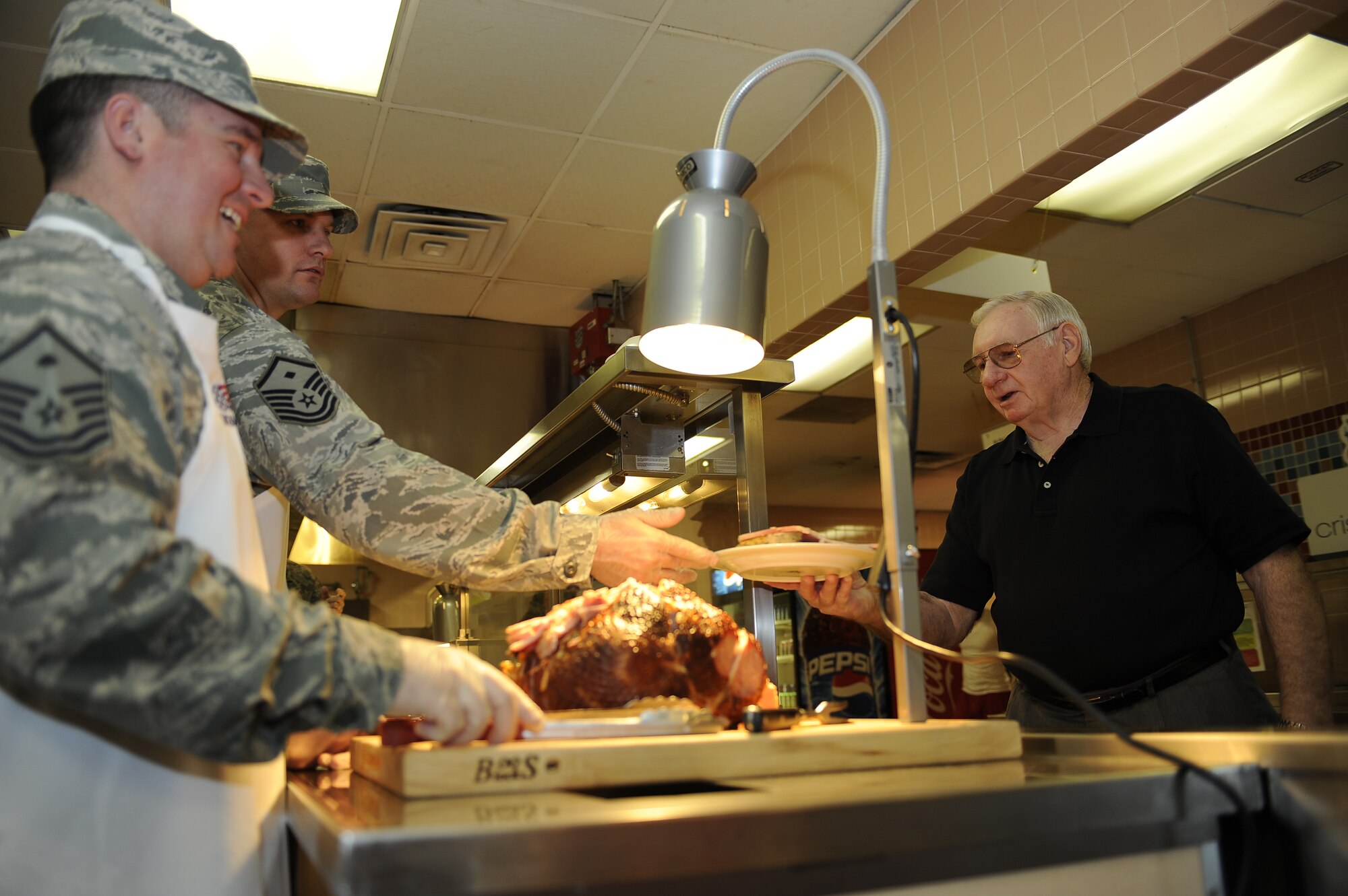 Master Sgt. Warren Benge, 57th Maintenance Squadron first sergeant, serves food to a guest at the Crosswinds Dining Facility during a holiday meal Dec. 25, 2013, at Nellis Air Force Base, Nev. The holiday meal was open to all active-duty military members, guardsmen, reservists, military retirees and their families. (U.S. Air Force photo by Airman 1st Class Timothy Young)