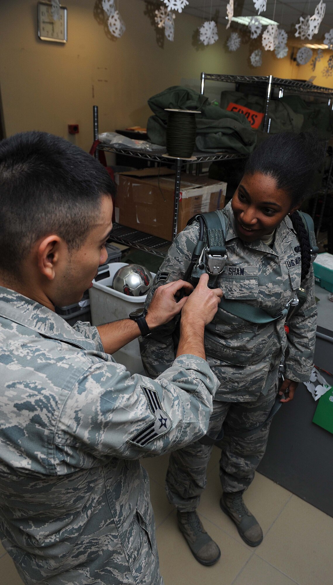Senior Airman Edvin Donis, 386th Expeditionary Operations Support Squadron assists Airman 1st Class Theda Shaw, 386th Expeditionary Force Support Squadron, with trying on a parachute during an Aircrew for a Day tour, undisclosed location, Southwest Asia. Donis is an aircrew flight equipment journeyman deployed from Quonset Air National Guard base, Rhode Island, native of Cumberland, Rhode Island. Shaw is a lodging clerk deployed out of Ramstein Air Base, Germany and is a native of Mansfield, Ohio. (U.S. Air Force photo by Senior Airman Desiree W. Moye)