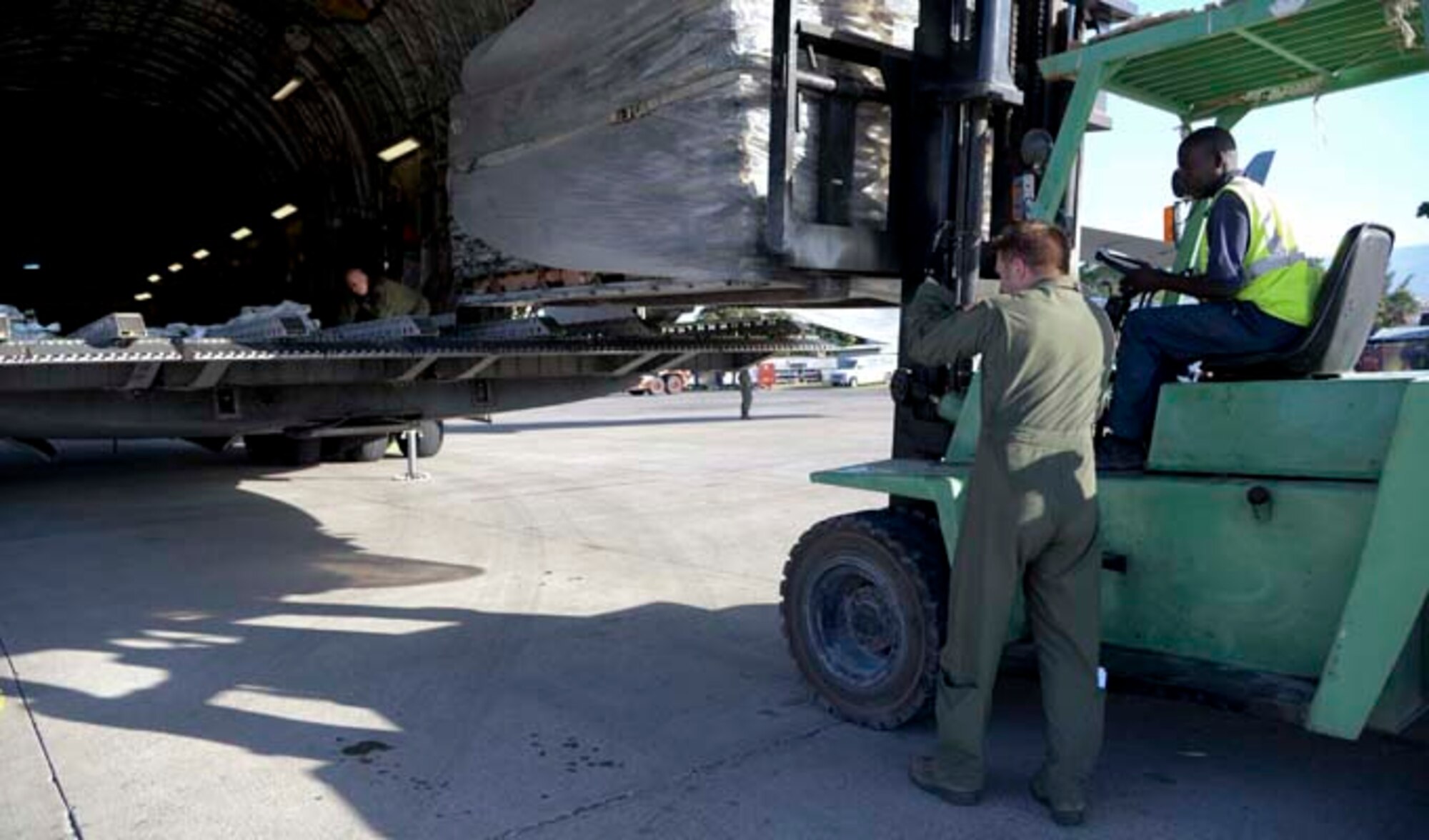 Tech. Sgt. William Hyde and Staff Sgt. Doug Tadevich help a Haitian citizen offload a pallet onto a forklift Dec. 19, 2013, at Port-au-Prince, Haiti. Airmen assigned to the 97th Air Mobility Wing delivered 136,000 pounds of rice, beans and corn meal that will be distributed to various orphanages in Haiti. Hyde is a 58th Airlift Squadron student training management flight chief and Tadevich is a 58th loadmaster instructor. (U.S. Air Force photo/Airman 1st Class Klynne Pearl Serrano)