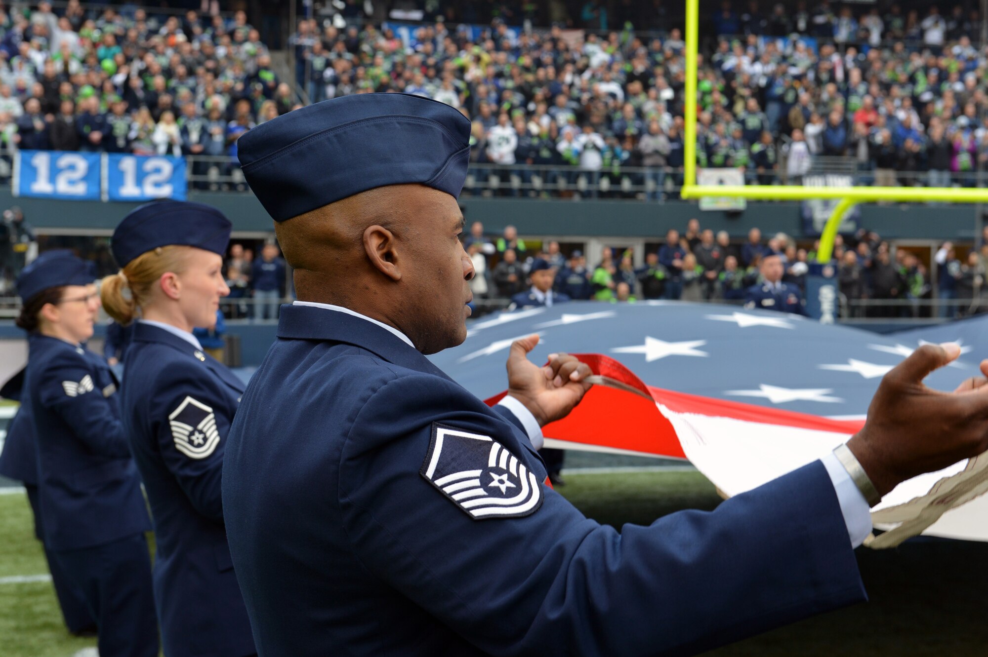Master Sgt. John Williams (front), 62nd Aircraft Maintenance Squadron, Master Sgt. Melissa Reimer (middle), 446th Aeromedical Staging Squadron and Staff Sgt. Melina Levesque (back), 62nd Airlift Wing, wave the U.S. flag up and down during the singing of the national anthem as part of the pregame ceremonies for the Seattle Seahawks final home game at CenturyLink Field in Seattle, Dec. 29, 2013. Team McChord Airmen worked together for the second time this season to present the colors at the Seahawks game. (U.S. Air Force photo/Master Sgt. Todd Wivell)