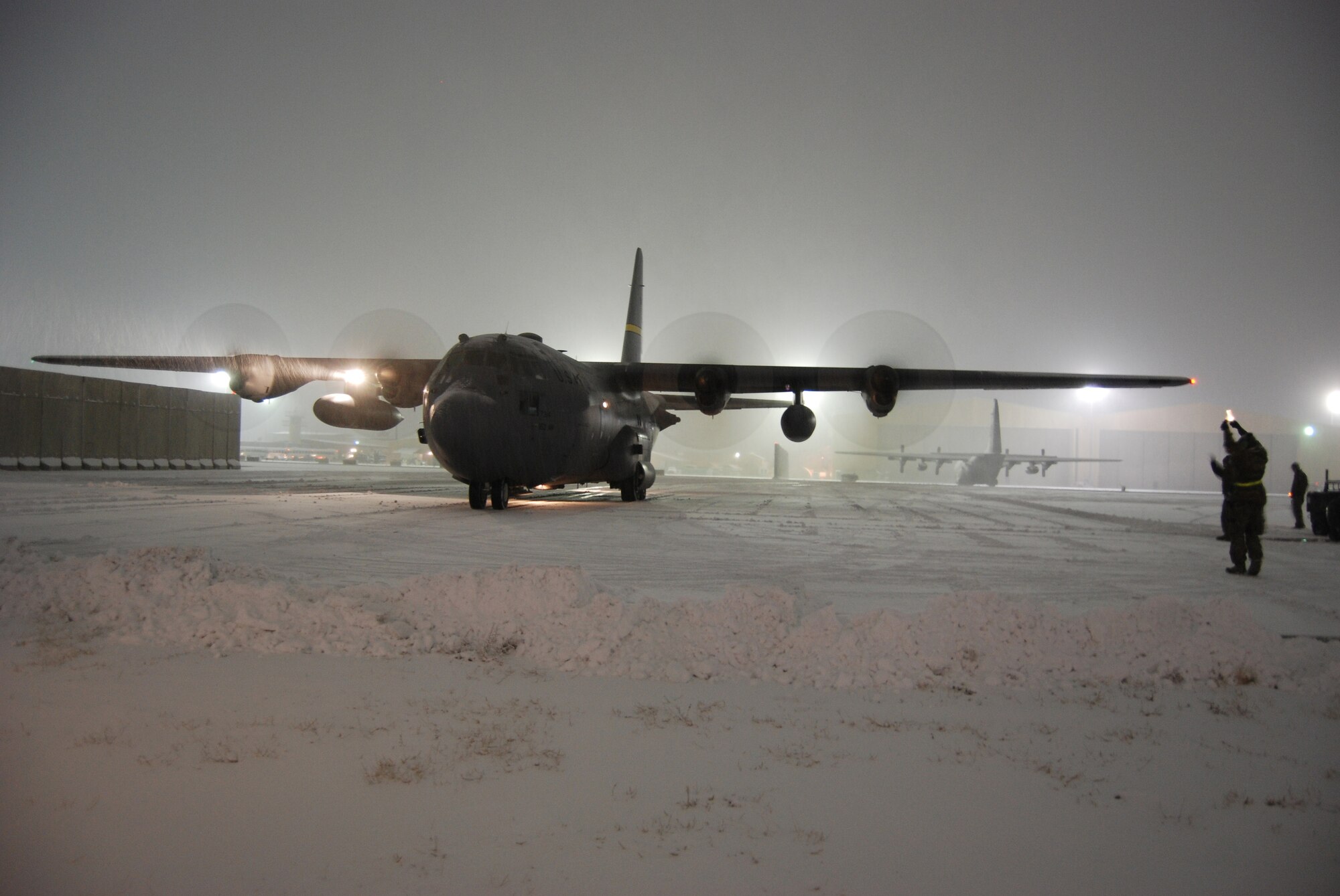 An Airman directs a C-130 Hercules into a parking spot during a snowstorm, Dec. 29, 2013 at Bagram Airfield, Afghanistan. Total snow accumulation was approximately 3 inches. (U.S. Air Force photo by Capt. Brian Wagner/Released)