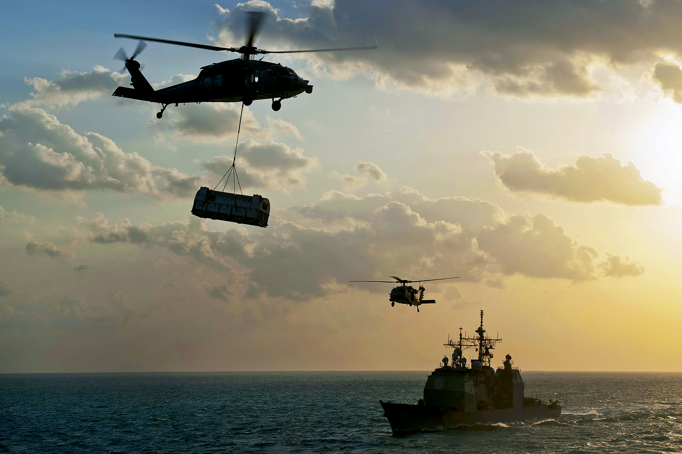 An Mh 60s Seahawk Helicopter Transports Supplies Over The Guided Missile Cruiser Uss Gettysburg During A