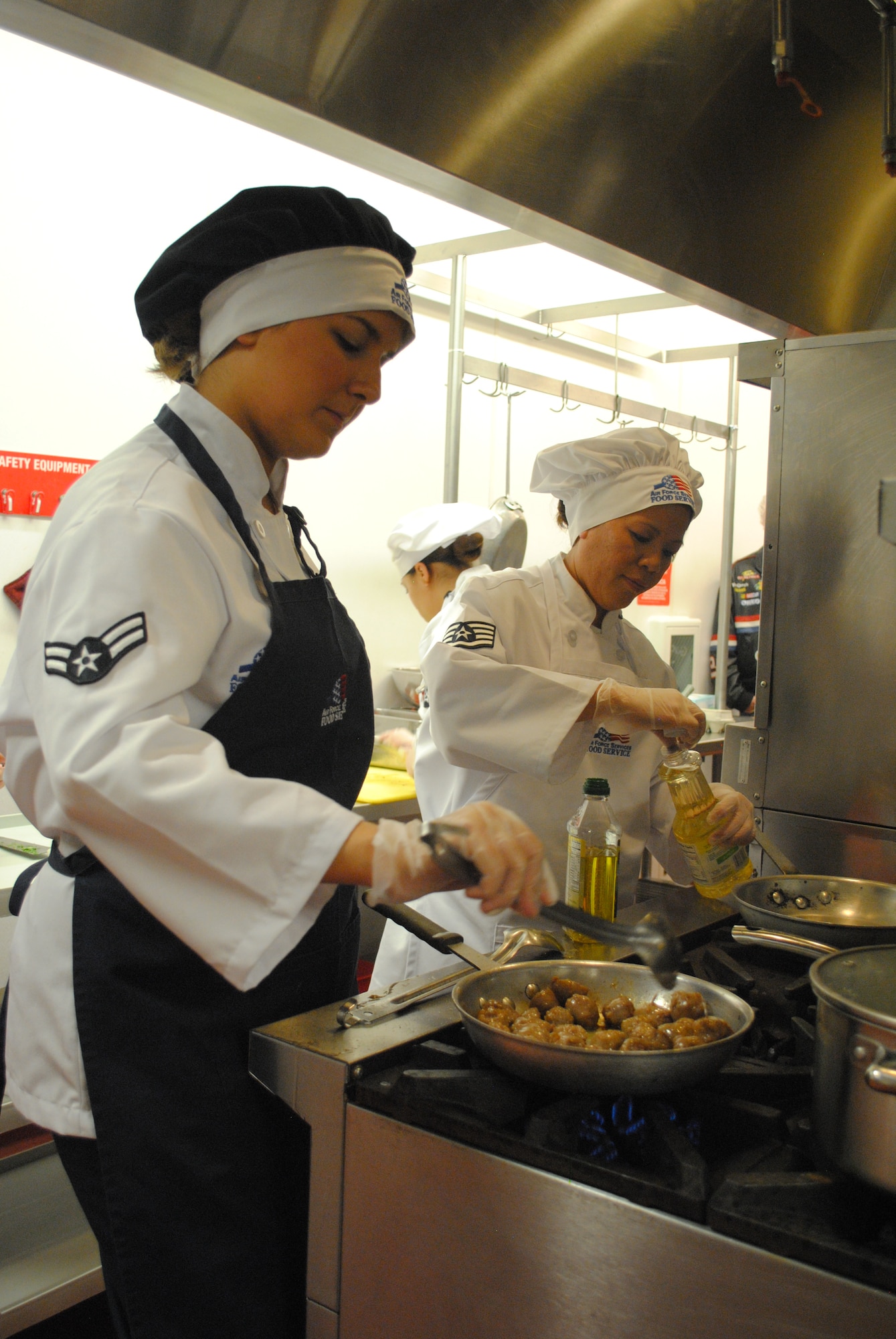 Airman 1st Class Gracie Vinson, 490th Missile Squadron chef, cooks meatballs in a skillet as Staff Sgt. Rowena Hawley, 341st Force Support Squadron food service supervisor, prepares a pan to cook island-style fried rice during the First Quarter Warrior Chef Competition at the Elkhorn Dining Facility on Jan. 25. (U.S. Air Force photo/Airman 1st Class Katrina Heikkinen)
