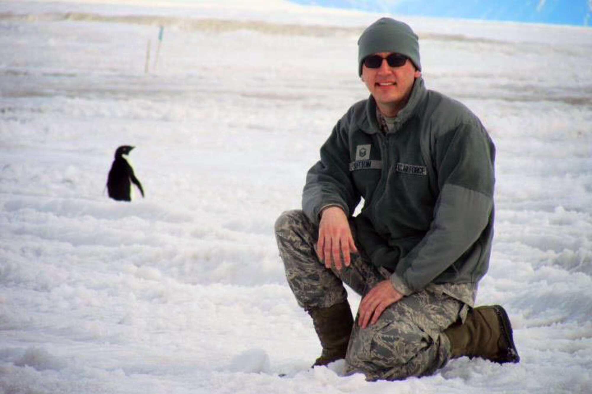 Master Sgt. Tyler Sutton, 176th Wing, Alaska Air National Guard, smiles while a penguin walks by the flight line near McMurdo Air Station, Antarctica. Sutton augmented the New York Air National Guard as an aircrew flight equipment specialist during a 30-day rotation in Antarctica supporting the National Science Foundation. Photo courtesy of Master Sgt. Tyler Sutton, 176th Wing, Alaska Air National Guard.