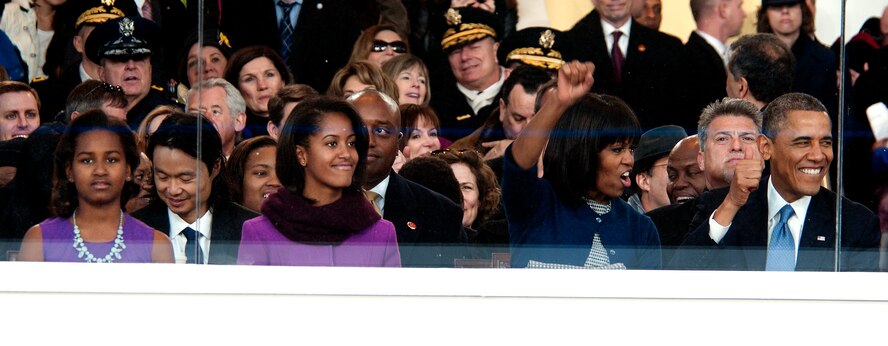 The Obama family cheers on a marching band from behind the reviewing stand glass during the 57th Presidential Inauguration parade in Washington, D.C., Jan. 21, 2013. As they enjoyed the entertainment of groups from all over the United States, National Guard members helped local and federal law enforcement keep people off of the parade route. (Air National Guard photo by Senior Airman Andrea F. Liechti)
