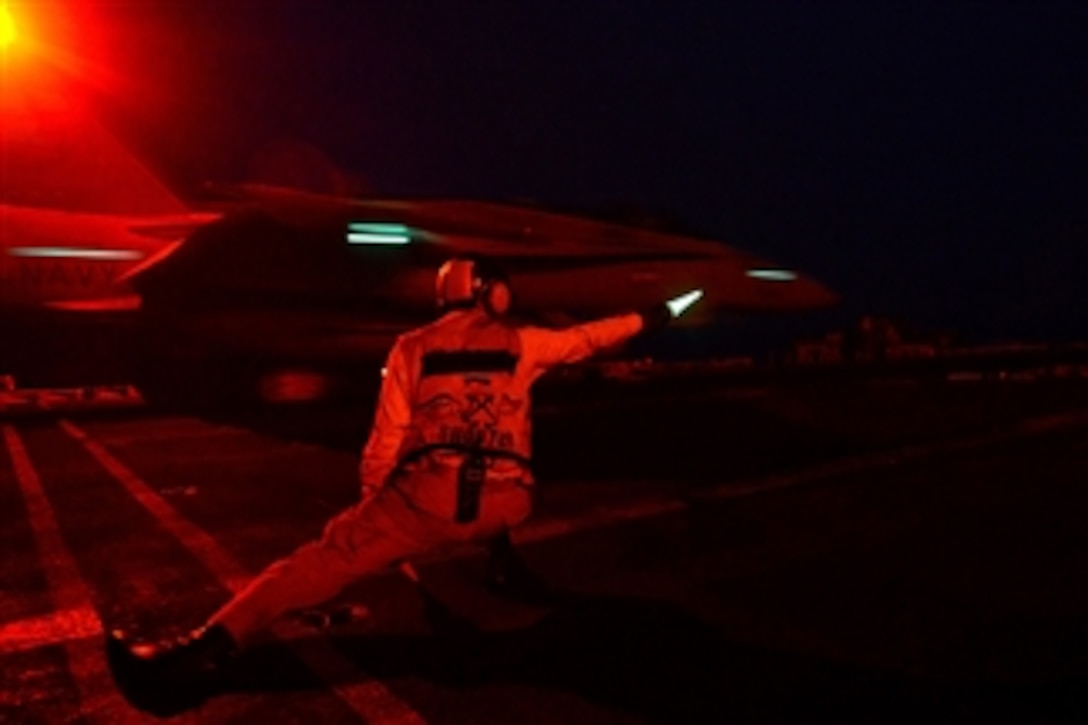 A catapult and arresting gear officer signals for the night launch of an aircraft from the aircraft carrier USS John C. Stennis (CVN 74) as the ship operates at sea on Jan. 31, 2013.  The Stennis is deployed to the 5th Fleet area of responsibility to conduct maritime security operations and theater security cooperation efforts.  