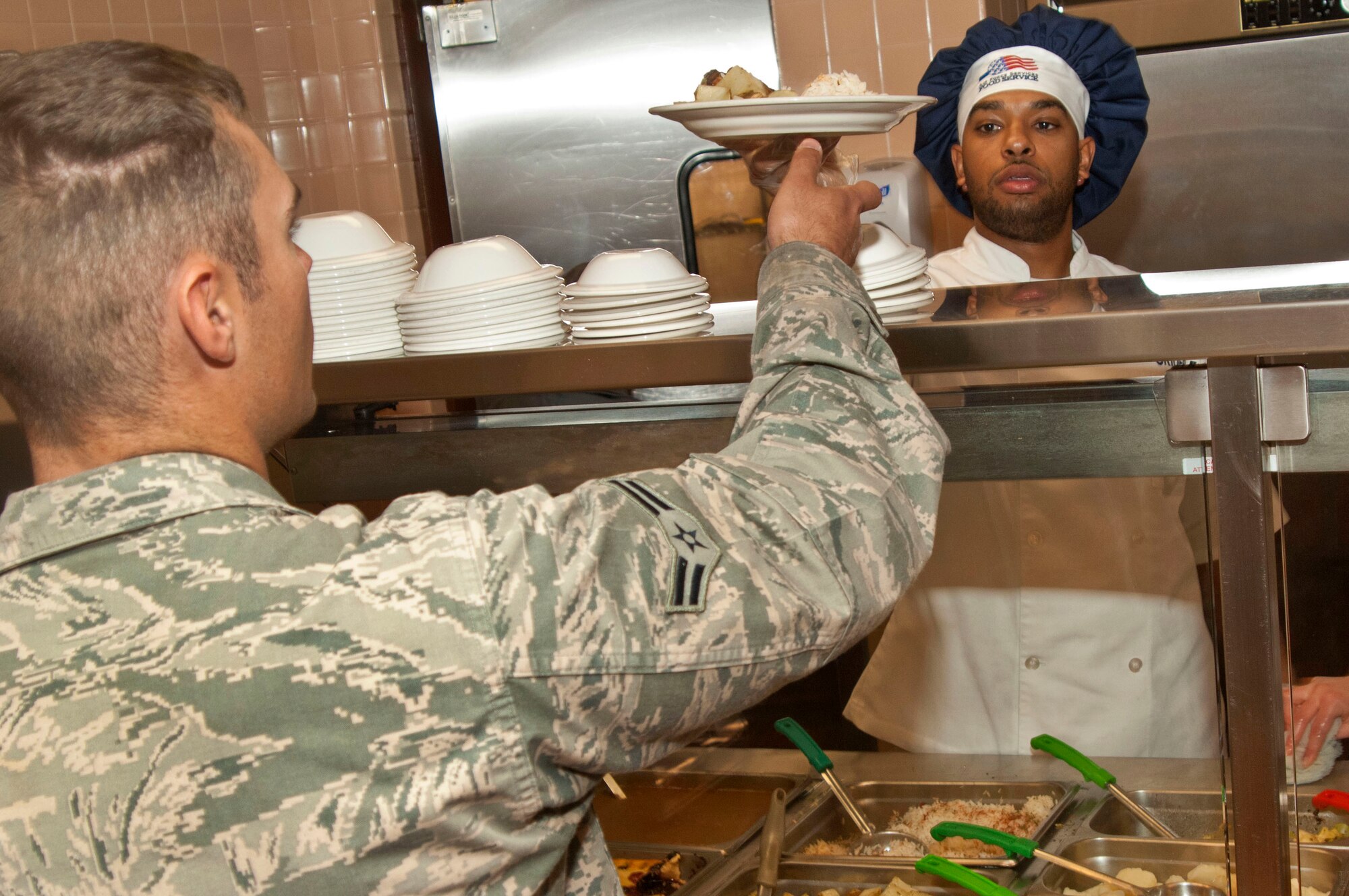 Senior Airman Anthony Crider, 99th Force Support Squadron services journeyman, hands a plate of food to an Airman during the lunch time rush at the Crosswinds Inn dining facility here Feb. 5. The 99th FSS food services are currently competing for the prestigious Hennessey Award that is awarded to the best Air Force dining facility. (U.S. Air Force photo by Airman 1st Class Monet Villacorte)