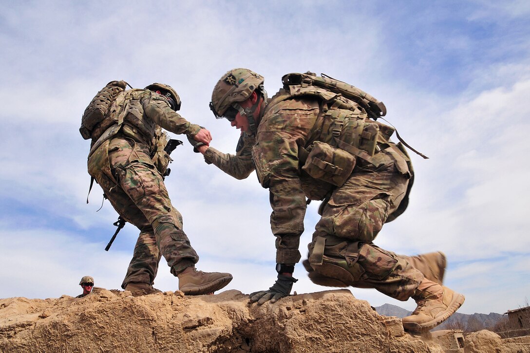 A U.S. soldier helps a fellow soldier onto the rooftop of an old, destroyed building to provide overwatch for another element of their patrol in the Panjwa’i district, Afghanistan, Jan. 29, 2013.