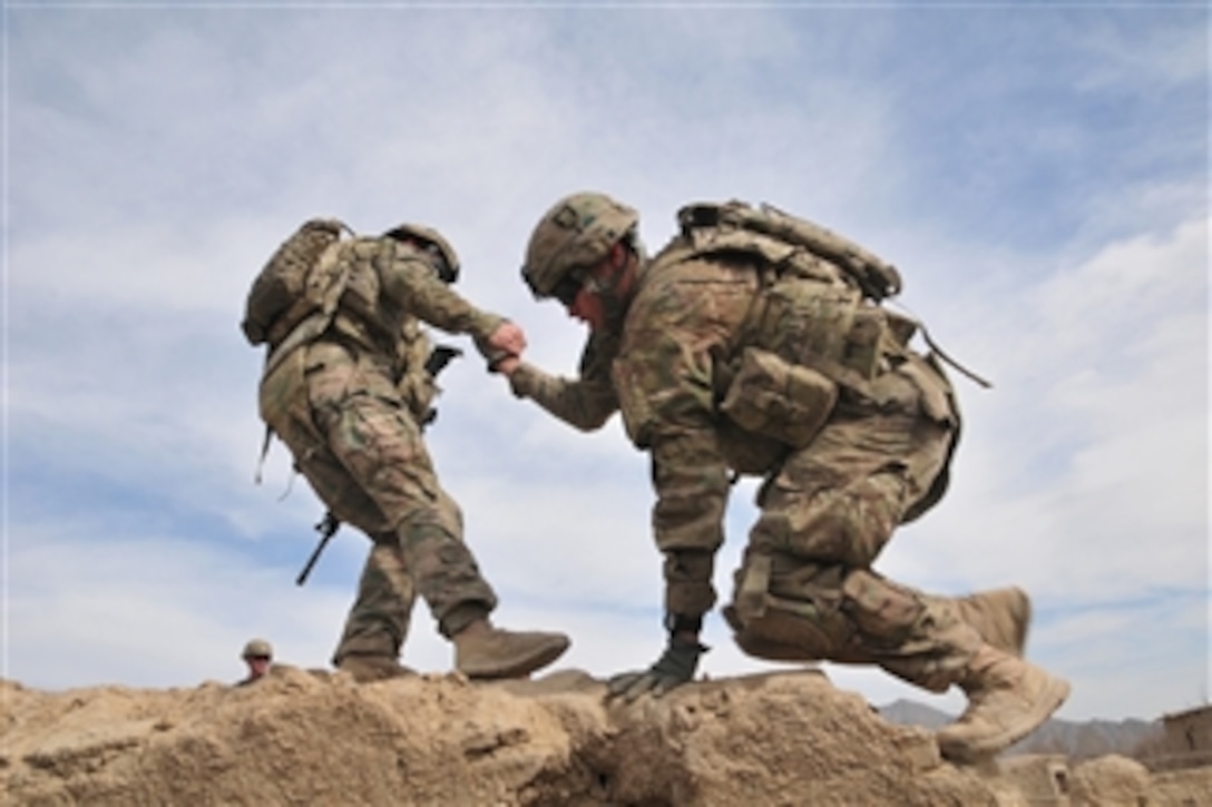 A soldier helps a fellow soldier onto the rooftop of an old building in order to provide protective over watch for another element of their patrol in the Panjwa’i District of Afghanistan on Jan. 29, 2012.  The soldiers are attached to the 1st Battalion, 38th Infantry Regiment, Combined Task Force 4-2 and are deployed to Afghanistan from Joint Base Lewis-McChord, Wash.  