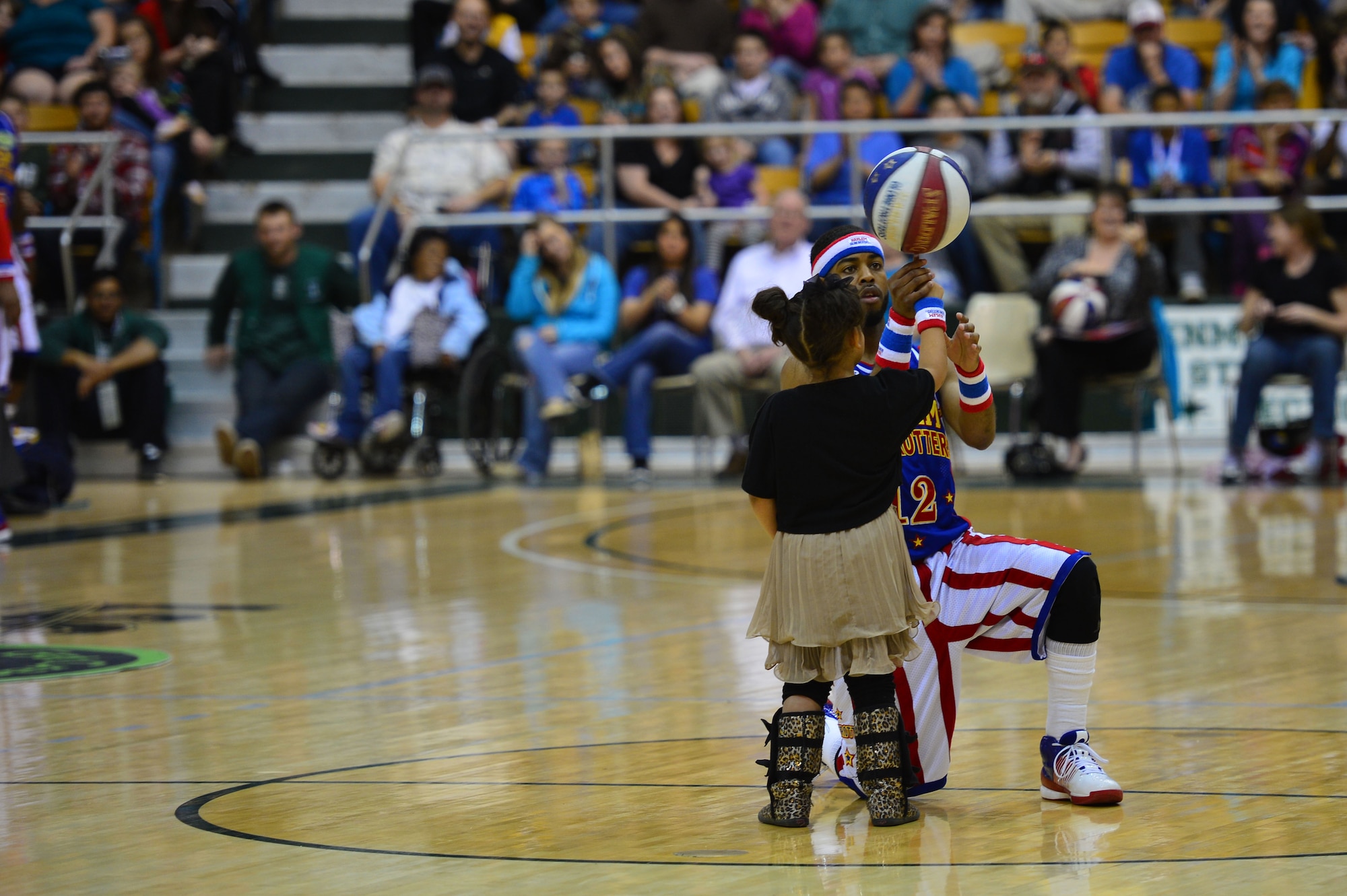 Ant Atkinson, guard for the Harlem Globetrotters, assists a young spectator with a basketball trick during an intermission of a basketball game at the Greyhound Arena in Portales, N.M., Feb. 5, 2013. The Harlem Globetrotters offered a crowd of several hundred people a comical, energy-packed game. (U.S. Air Force photo/Airman 1st Class Eboni Reece)