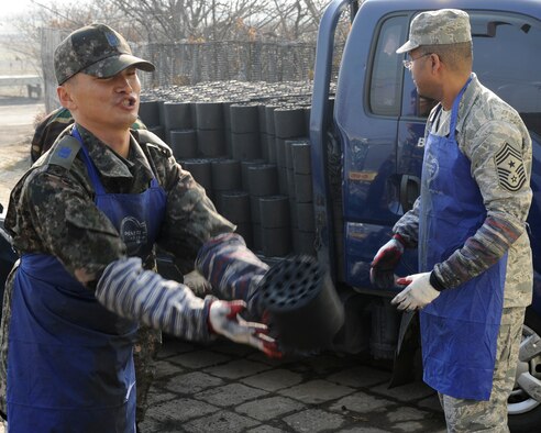 Republic of Korea Air Force Chief Master Sgt. Ki Yul Kim, 38th Fighter Group command chief, left, tosses a coal briquette to other volunteers, as CMSgt Phillip Robinson, 8th Fighter Wing command chief, waits his turn at Gunsan City, Republic of Korea, Jan. 30, 2013. The coal was donated to needy families to heat their homes. (U.S. Air Force photo by Senior Airman Marcus Morris/Released)