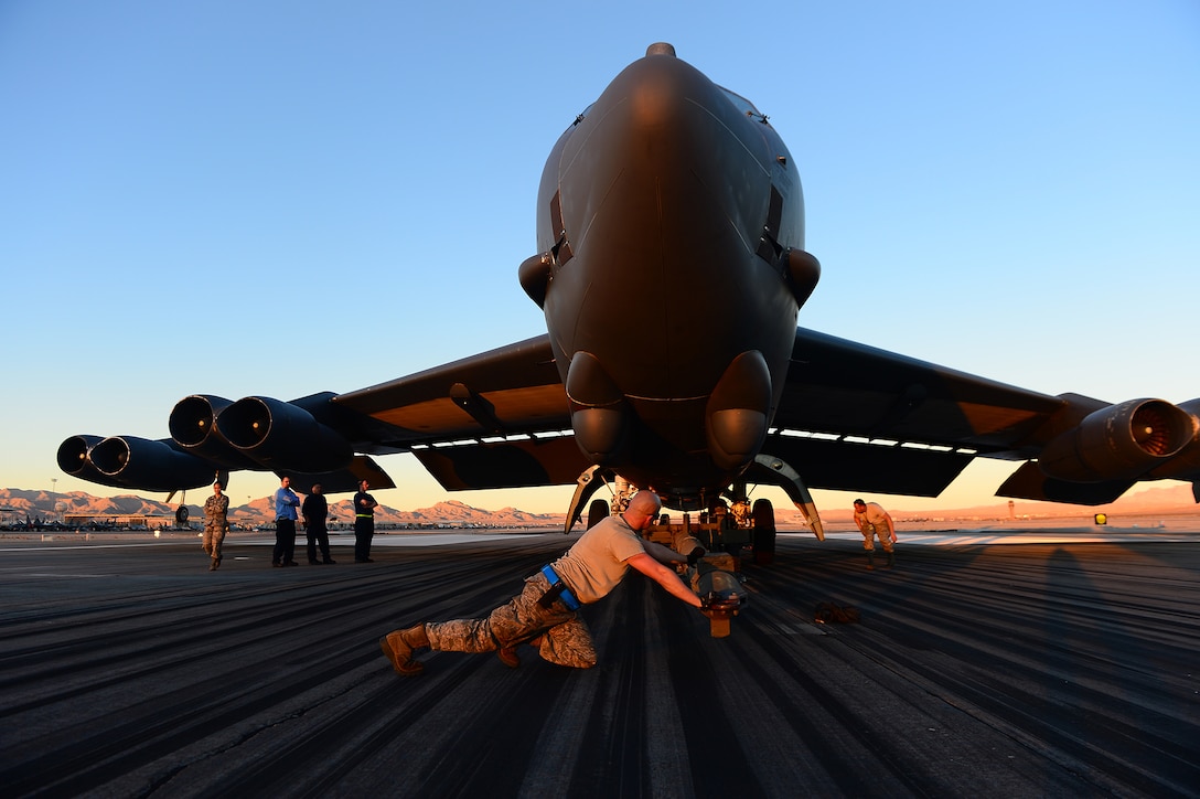 Air Force Senior Airman John Myer pushes a tow bar under the tire of a B-52H Stratofortress at Nellis Air Force Base, Nevada. 