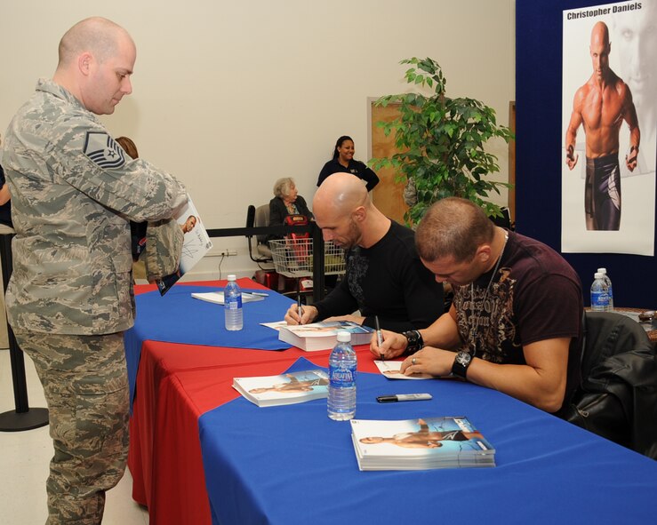 Total Non-Stop Action Impact wrestlers, Christopher Daniels and Frankie Kazarian, sign autographs for Master Sgt. Kenneth Shea, Air Force Global Strike Command, at the Base Exchange on Barksdale Air Force Base, La., Feb. 8. While in town for their upcoming show, Daniels and Kazarian met with Team Barksdale to sign autographs and pose for pictures. (U.S. Air Force photo/Senior Airman Sean Martin)