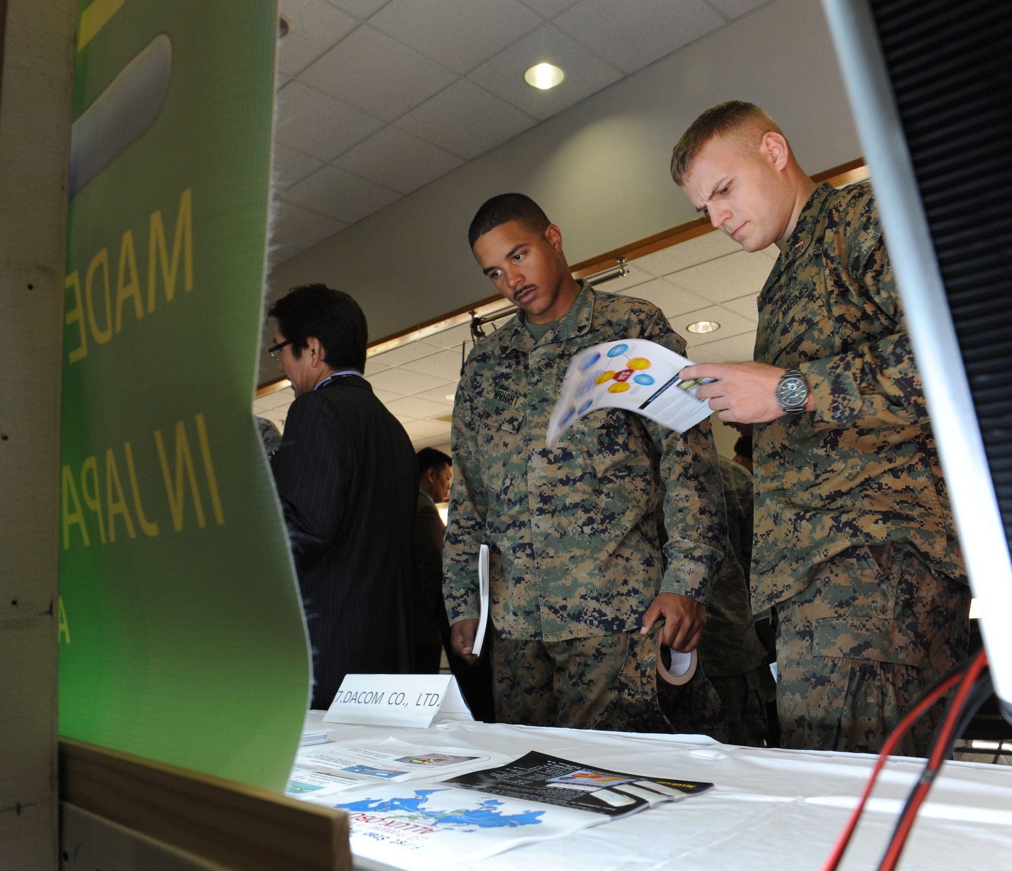 U.S. Marine Corps 1st Lt. Carl Anderson, 3rd Maintenance Battalion supply officer, and Cpl. Richard Wright, 3rd Maintenance Battalion administrative NCO, look at the DACOM Company display at the third-annual Okinawan first vendor showcase on Kadena Air Base, Japan, Feb. 7, 2013. Some products DACOM Company sells are toner and ink cartridges, light-emitting diode lighting and a drum for laser printers. (U.S. Air Force photo/Airman 1st Class Malia Jenkins)