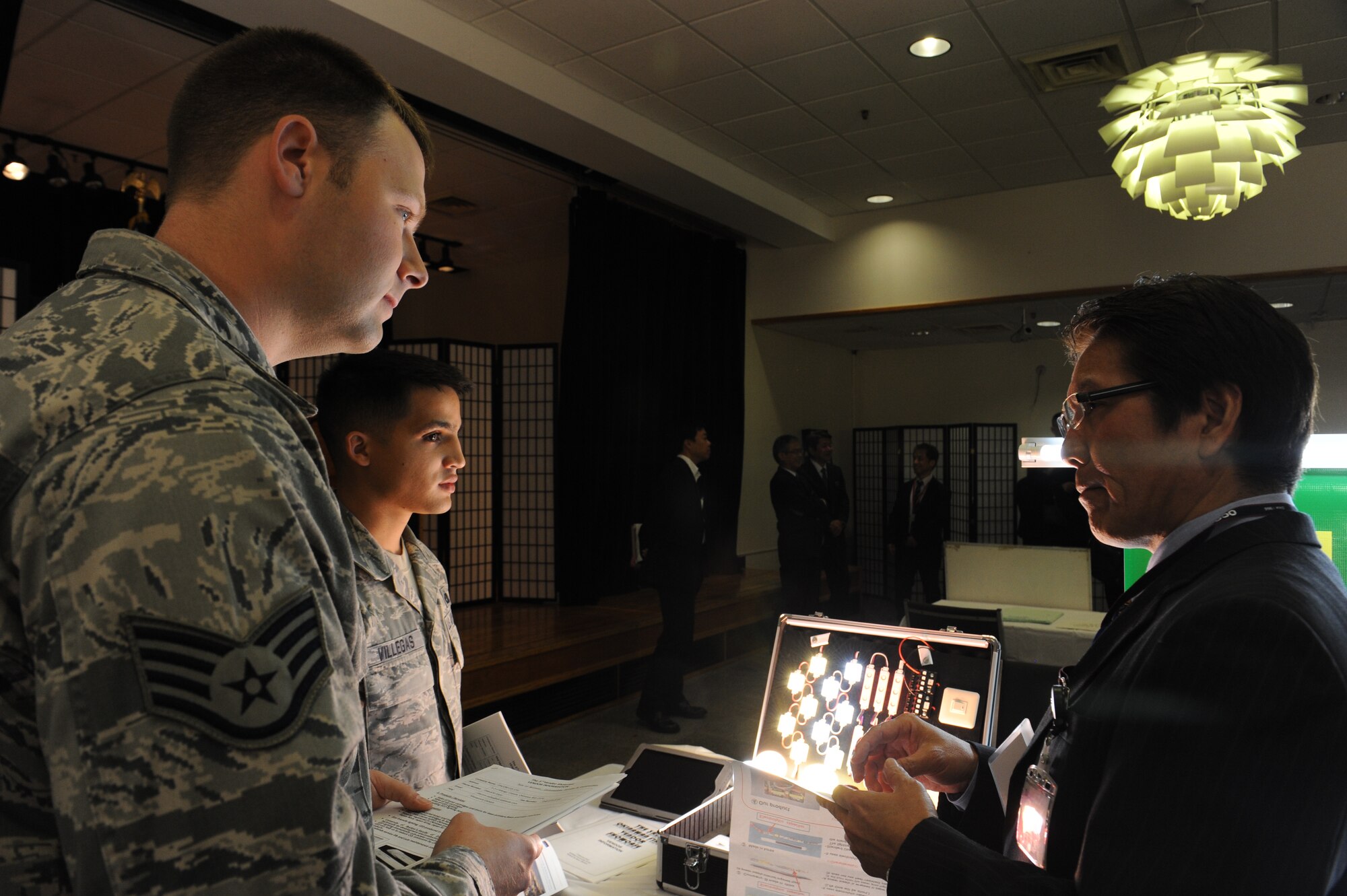 U.S. Air Force Staff Sgts. Douglas Cummings, 18th Component Maintenance Squadron avionics team leader, and Carlos Villegas, 18th CMS resource advisor, talk to Masayoshi Uehara, a DACOM company member, at the third-annual Okinawan first vendor showcase on Kadena Air Base, Japan, Feb. 7, 2013. The showcase allowed service members to view products from local companies to provide units alternatives when ordering supplies and to foster goodwill with the local community. (U.S. Air Force photo/Airman 1st Class Malia Jenkins)