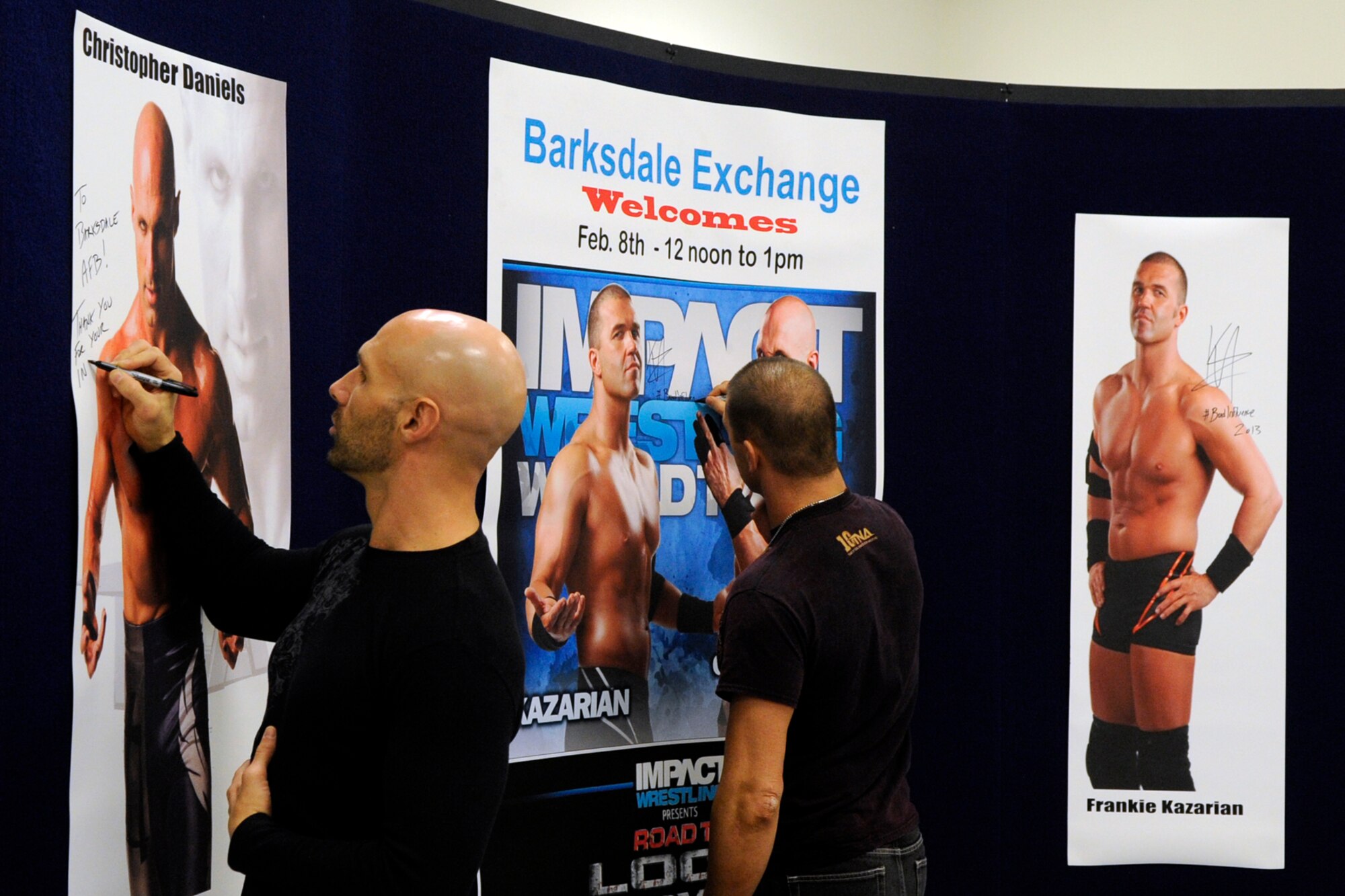 Total Nonstop Action wrestlers, Christopher Daniels and Frankie Kazarian sign posters for fans at a meet and greet session at the Barksdale Exchange on Barksdale Air Force Base, La., Feb. 8, 2013. The two wrestlers competed during the Road to Lock Down event at the Centurylink Center in Bossier City, La., Feb. 8. (U.S. Air Force photo by Master Sgt. Jeff Walston)