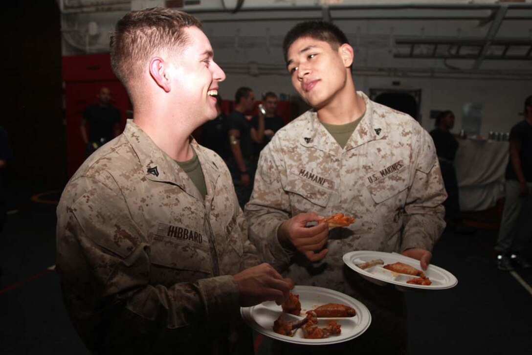 Corporals Christopher W. Hibbard (left), assessment consequence management team member, Chemical Biological Radiological Nuclear Defense Detachment, and Jose M. Mamani, supply clerk, both with the Command Element, 15th Marine Expeditionary Unit, eat chicken wings during the Super Bowl party held in the hangar bay of the USS Peleliu, Feb. 4. The ship hosted a Super Bowl party for its Marines and sailors as a way to help them decompress and enjoy some of the comforts of home while being forward deployed. The 15th MEU is deployed as part of the Peleliu Amphibious Ready Group as a U.S. Central Command theater reserve force, providing support for maritime security operations and theater security cooperation efforts in the U.S. 5th Fleet area of responsibility. Hibbard, 25, is from Mexia, Texas, and Mamani, 21, is from Burke, Va.