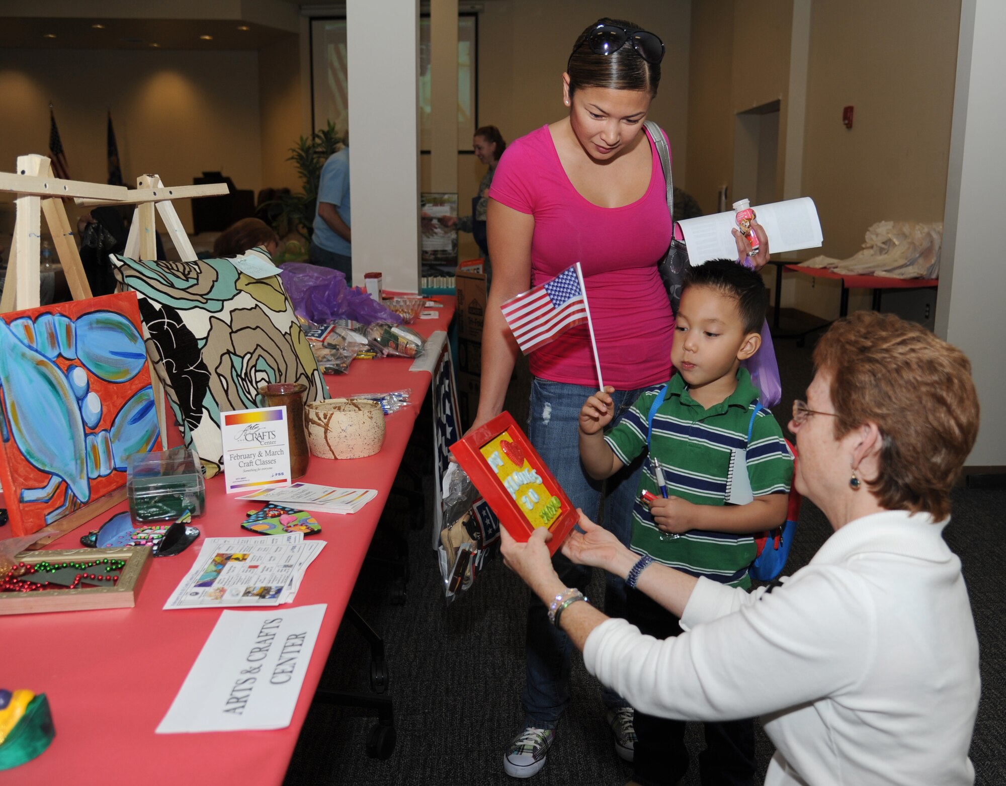 Tech. Sgt. Triscia Garcia, 334th Training Squadron, watches as her son Christian, 4, is shown a piece of art by Debra Pearson, Arts and Crafts Center director, during the military preparedness exposition Feb. 7, 2013, at the Roberts Consolidated Aircraft Maintenance Facility.  Various agencies set up information displays and booths to assist those who have recently returned from a deployment or will soon be deploying.  (U.S. Air Force photo by Kemberly Groue)