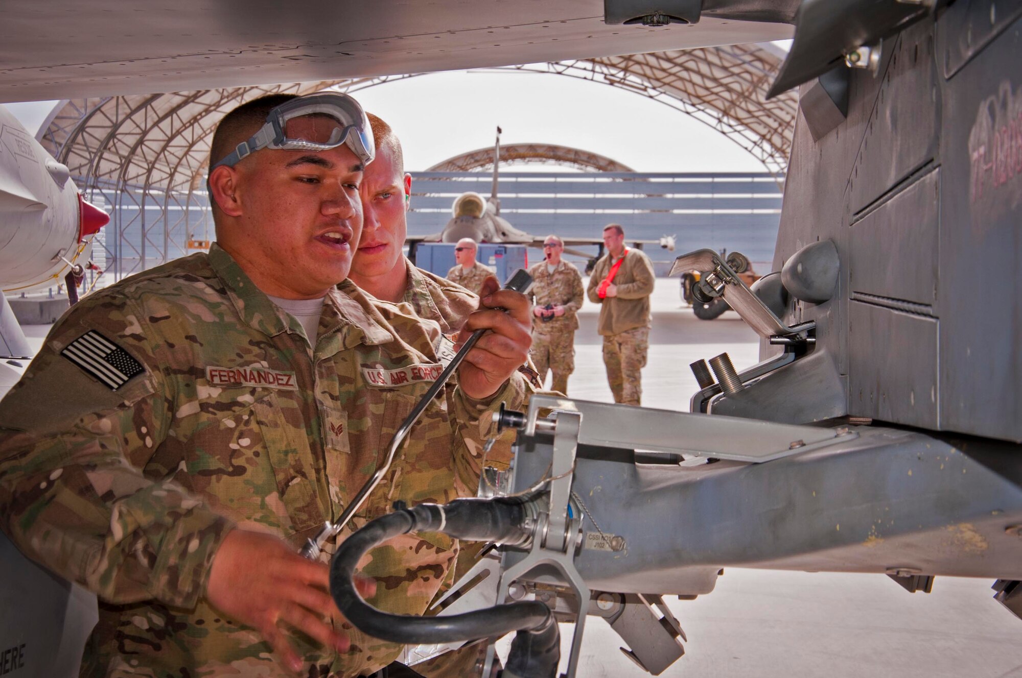 KANDAHAR AIRFIELD, Afghanistan -- Senior Airman Kameran Fernandez, 451st Expeditionary Aircraft Maintenance Squadron weapons load crew member, preps a BRU-57 bomb rack as an evaluator looks on during a weapons load competition here Feb. 11. Fernandez and two other Airmen made up a three-man weapons load crew and completed a four-phase evaluation. Their overall score will be put up against other scores of weapons load crews from their home station, Shaw Air Force Base, S.C.  (U.S. Air Force photo/Senior Airman Scott Saldukas)
