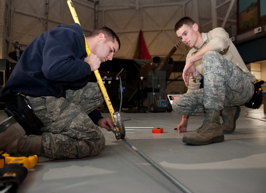 Senior Airman Josh Smith (left),and Airman 1st Class Alexander Price, 28th Civil Engineer Squadron electrical systems technicians, position an electrical wire conduit pipe at the South Dakota Air and Space Museum, Box Elder, S.D., Jan. 30, 2013. The SDASM is replacing all light fixtures with Light-Emitting Diode lights to increase the energy efficiency of the building. (U.S. Air Force photo by Airman 1st Class Alystria Maurer/Released)
