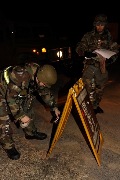 Airman 1st Class Cody Colbaugh, left, 8th Communications Squadron, sets up a stanchion while Airman 1st Class Joseph Pandolfo, 8th CS, confirms the zone during exercise Beverly Bulldog 13-2 at Kunsan Air Base, Republic of Korea, Feb. 12, 2013. The stanchions list the necessary MOPP level precautions for Airmen as they enter or leave a chemical zone. (U.S. Air Force photo by Senior Airman Marcus Morris/Released)