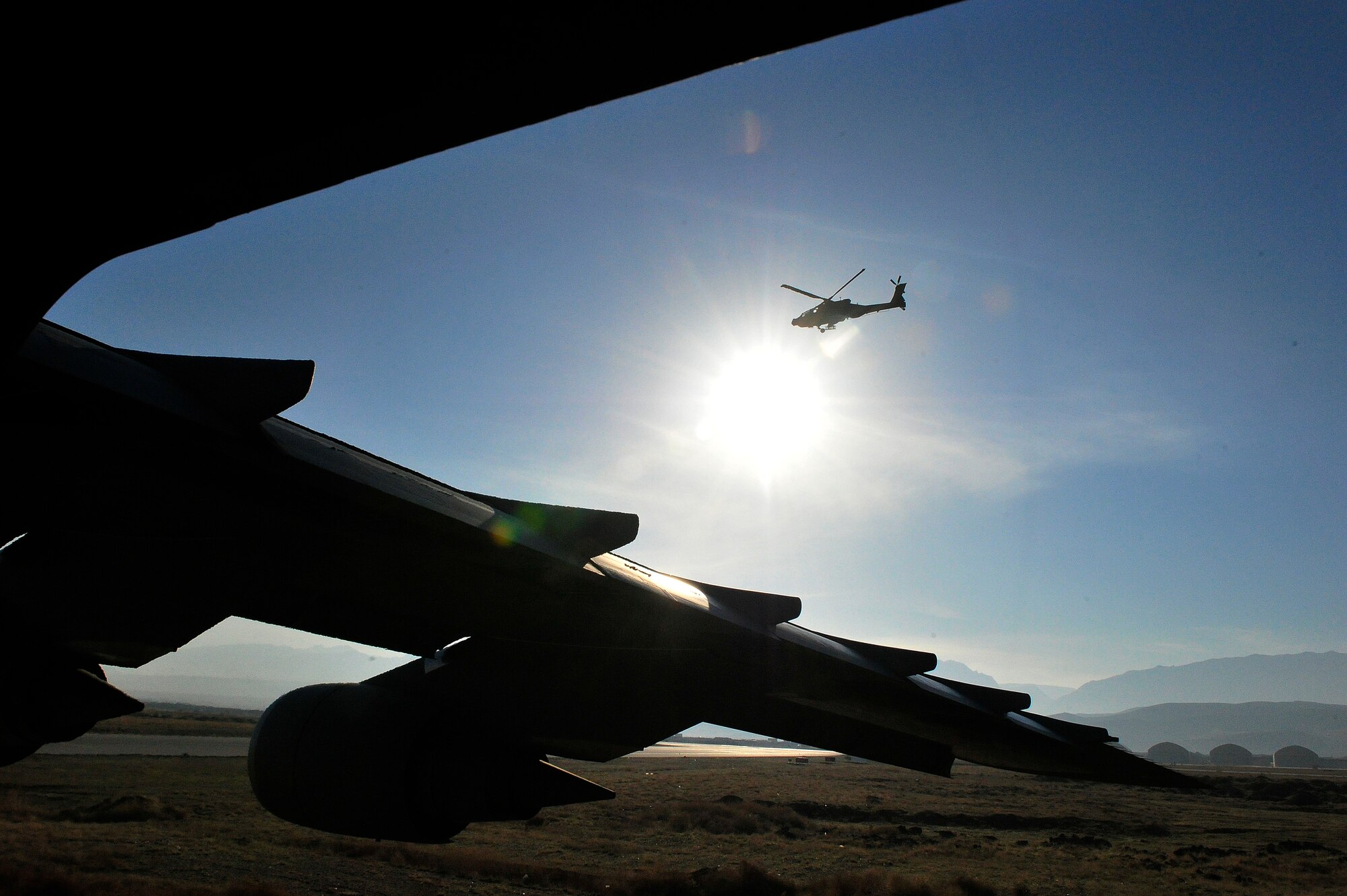 CAMP MARMAL, Afghanistan – A U.S. Army AH-64 Apache helicopter flies past a 436th Airlift Wing C-5M Super Galaxy here Jan. 28, 2013. The 621st sent a contingency response team to Mazar-e-sharif Afghanistan to provide en-route command and control and communications support in support of a U.S. transportation command intermodal movement of two U.S. Army Combat Aviation Brigades. (U.S. Air Force photo by Tech Sgt. Parker Gyokeres)