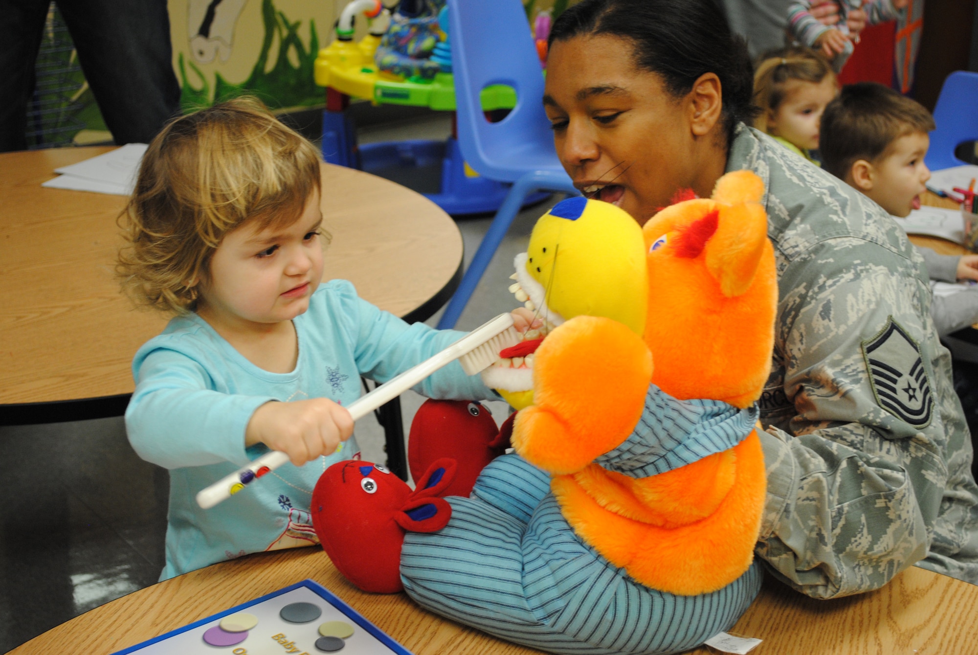 Master Sgt. Shanaya Fournier, 319th Medical Operations Squadron Dental Flight NCO in-charge, helps 2-year old Ellie Pagel brush Rex the Dental Health Mascot’s teeth during Feb. 12, 2013, visit to the Parent Child Center on Grand Forks Air Force Base, N.D.  The visit by three dental health experts was done in observance of National Children's Dental Health Month, a nation-wide campaign endorsed by the American Dental Association designed to promote awareness about the importance of oral health. (U.S. Air Force photo/Senior Airman Luis Loza Gutierrez)