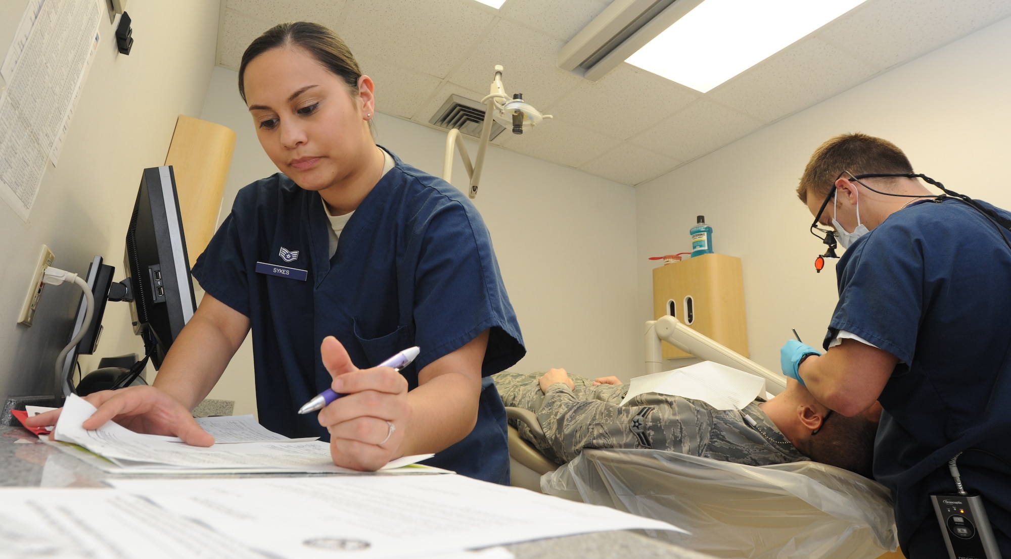 WHITEMAN AIR FORCE BASE, Mo. -- Staff Sgt. Jessica Sykes, 509th Medical Operations Squadron dental technician, writes up an entry for a patient record as Dr. (Capt.) Nicholas Polczynski, 509th MDOS dentist, performs an exam, Feb. 4. It costs the 509th MDOS an average of $2.6 million to take care of dental appointments each year. (U.S. Air Force photo/Staff Sgt. Nick Wilson) (Released)