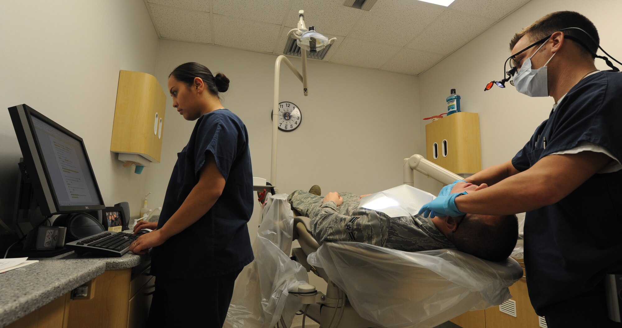WHITEMAN AIR FORCE BASE, Mo. -- Staff Sgt. Jessica Sykes, 509th Medical Operations Squadron dental technician, types up an entry for a patient record as Dr. (Capt.) Nicholas Polczynski, 509th MDOS dentist, performs an exam, Feb. 4. The entry Sykes is typing update’s the patients personal information in the dental flight’s medical records database. (U.S. Air Force photo/Staff Sgt. Nick Wilson) (Released)