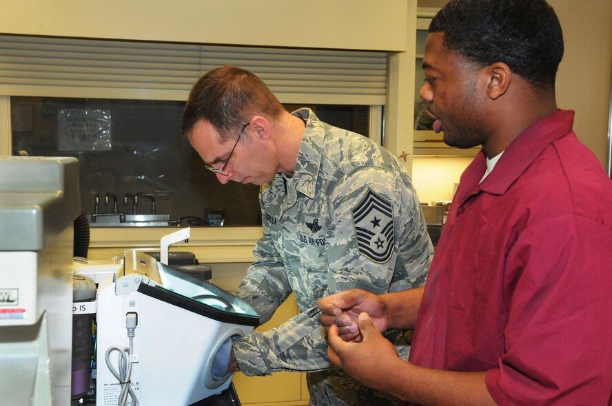 MINOT AIR FORCE BASE, N.D. -- Chief Master Sgt. Kevin Jurgella, 5th Bomb Wing command chief, receives instructions from Senior Airman Justin Phillips, 5th Medical Group dental lab technician, during his visit to the 5th MDG Dental Lab here recently. The Dental Lab is a two-man section, but is currently only manned by one Airman. The lab is where all dental appliances and prosthetics are fabricated. Dental lab technicians are their own separate career field (4Y0X2), but fall under the management of the base dental clinic. The technician works closely with dental assistants and dentists to ensure patients receive the best care possible. Of all patient dental appliances, 99 percent are created here on base. The remaining 1 percent is sent out to the Area Dental Laboratory. (Photo courtesy of the Command Chief's Office)