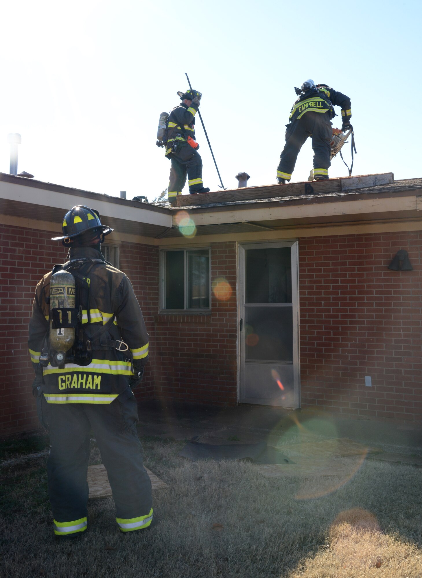 Firemen ventilate the roof of the smoke-filled Fire Safety House during a routine exercise Monday. The fire department on base practices fire drills at least once a week, varying the level of difficulty, the size of crews they use and the size of building in which they will be working. In this week’s exercise, the firemen did a primary fire attack on the structure, searched for victims, ventilated the fire room and attacked the blaze.  (Air Force photo by Kelly White)